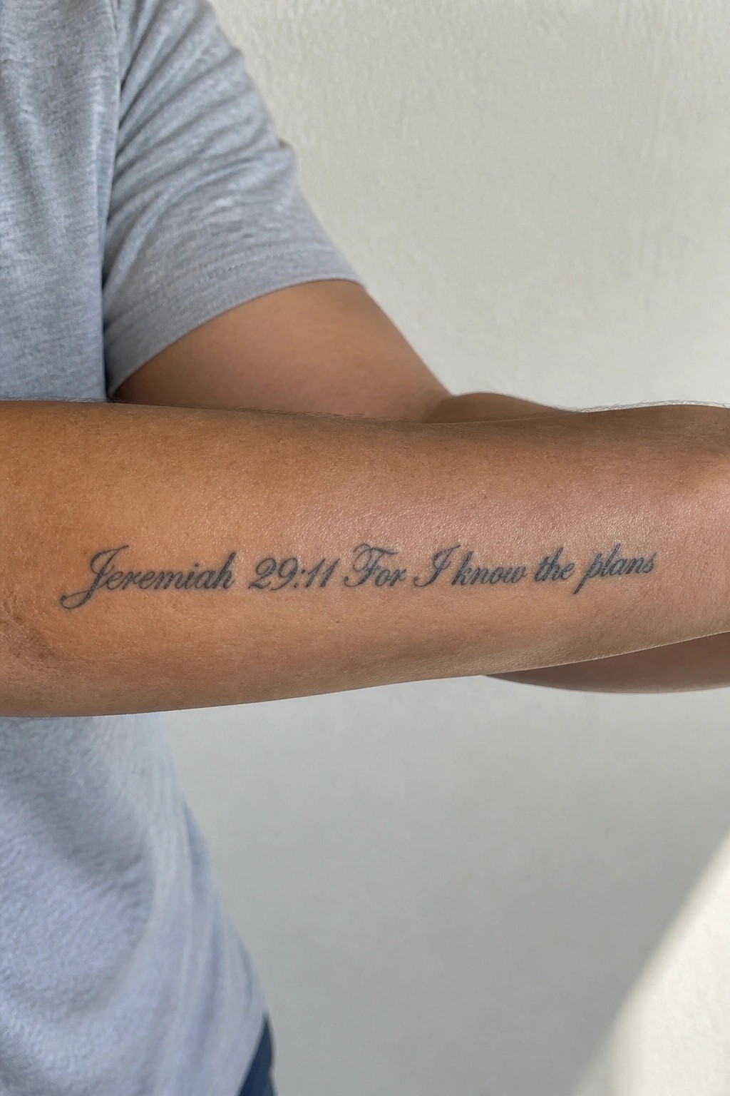 Gray t-shirt sleeve and forearm with cursive tattoo
