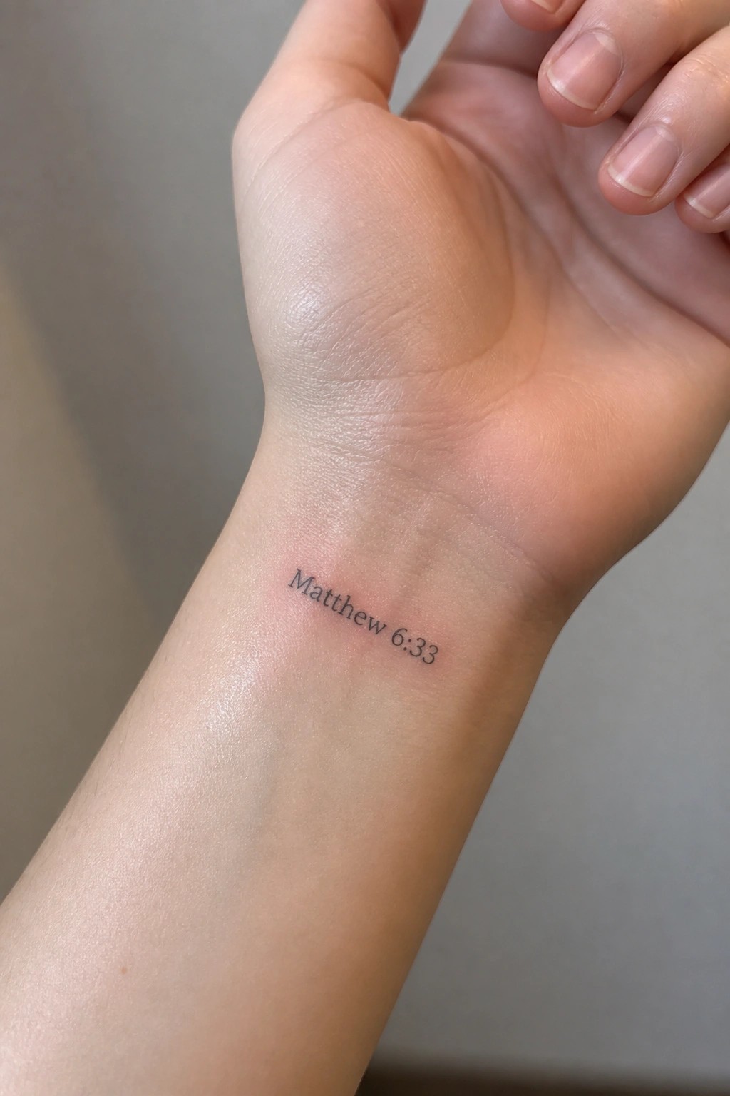 Close-up of light-skinned wrist with small black tattoo reading Matthew 6:33