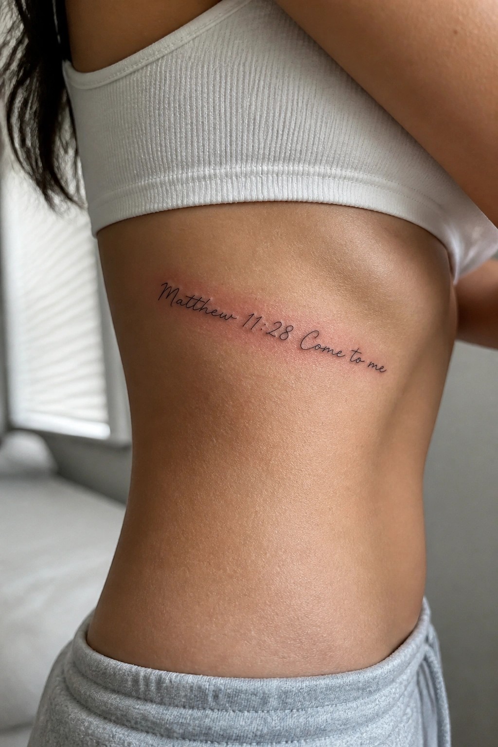 Minimalist cursive tattoo of Matthew 11:28 across the side torso under the arm