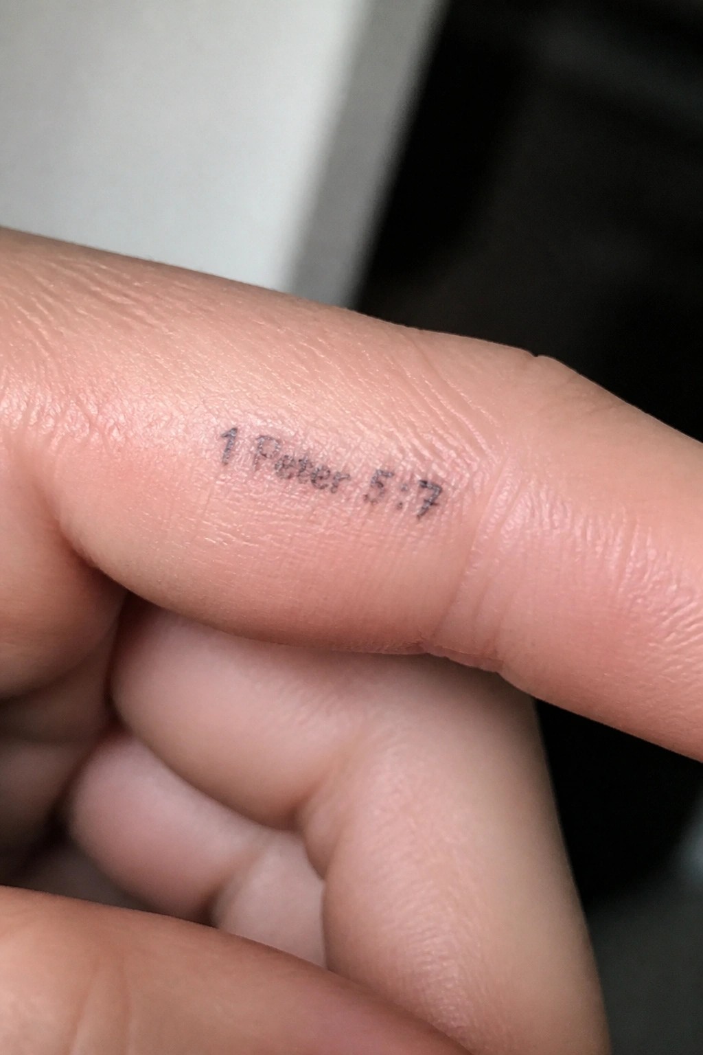 Close up of a finger with the text 1 Peter 5:7 tattooed in small black letters along the side.