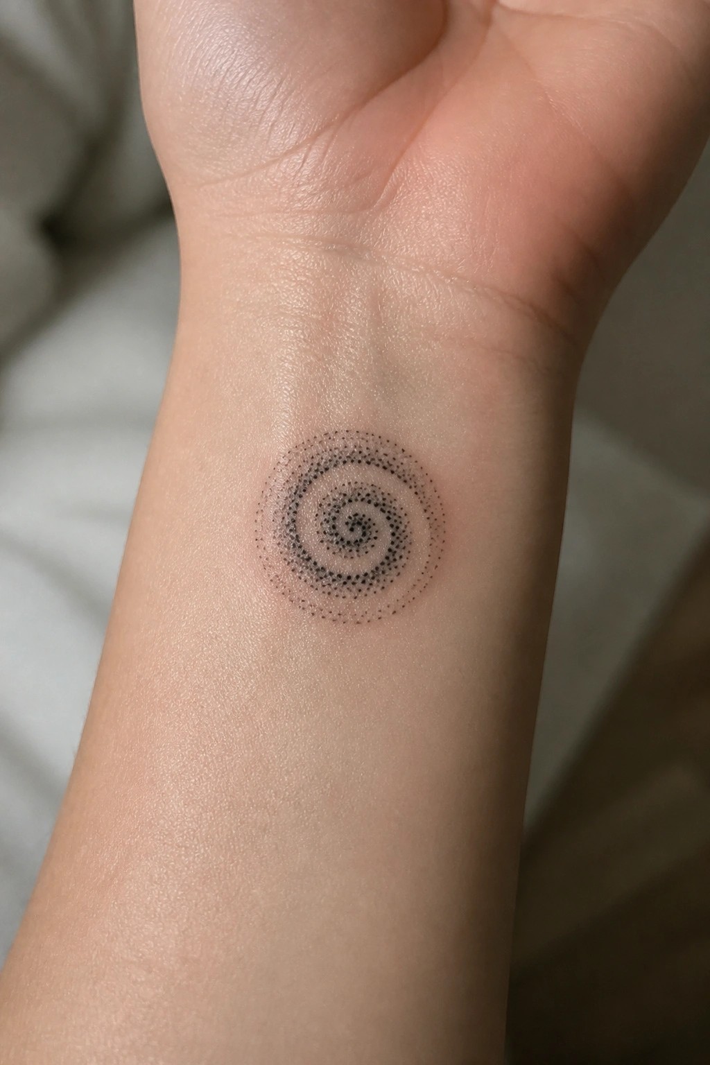 Small black dotwork spiral tattoo on the inner wrist