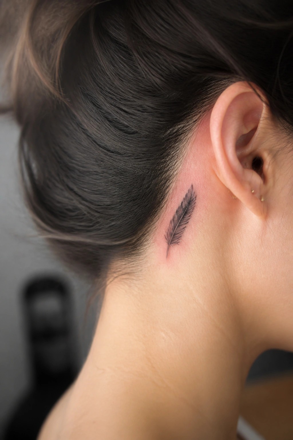 Close-up of dark hair in a bun with small black feather tattoo on reddened neck.