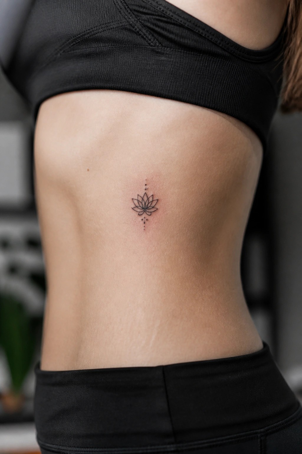 Woman's midriff in black top with small lotus tattoo on ribs.