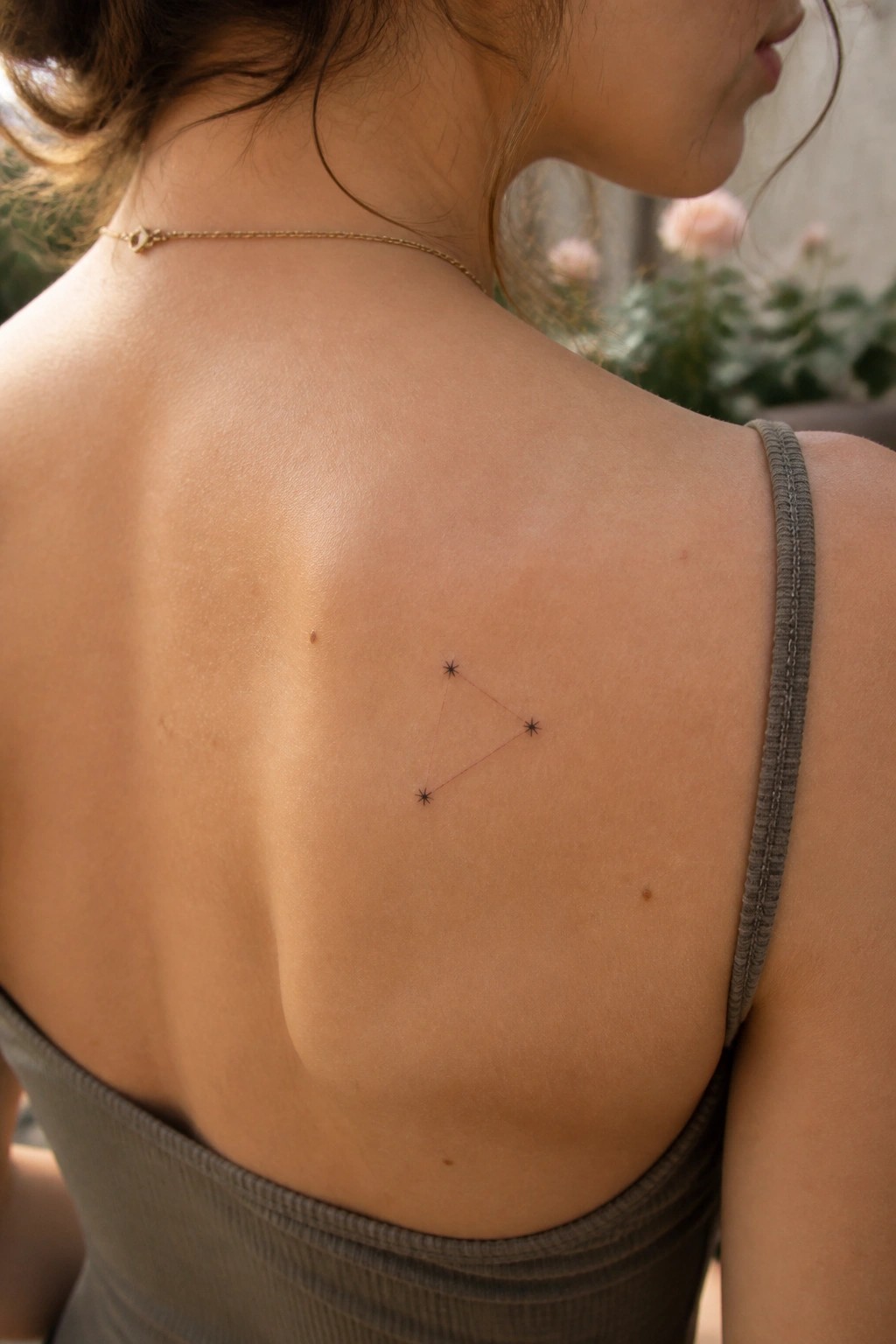 Woman's upper back with constellation tattoo above gray tank top and gold necklace