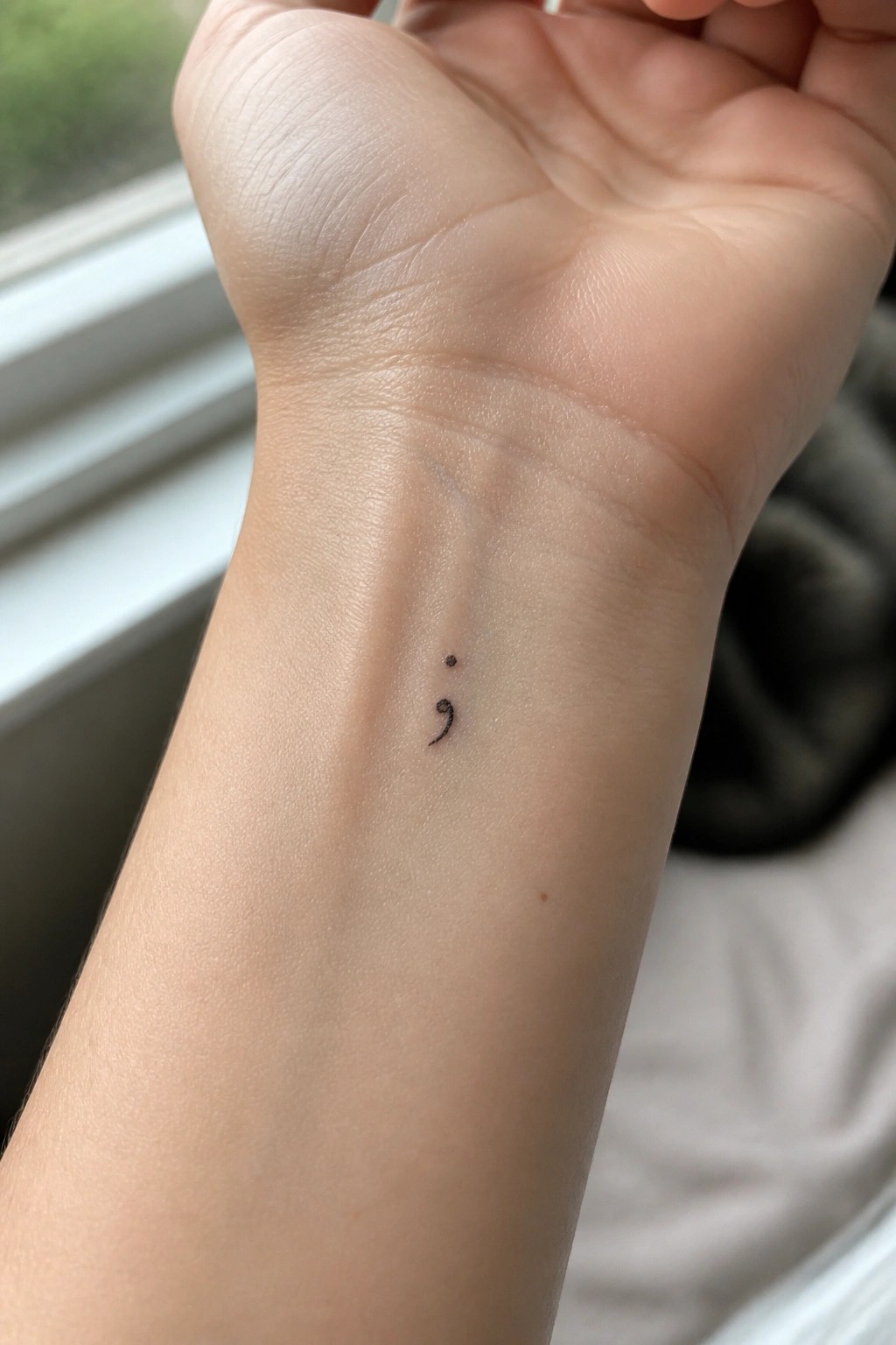 Light-skinned wrist with small black semicolon tattoo on inner forearm.