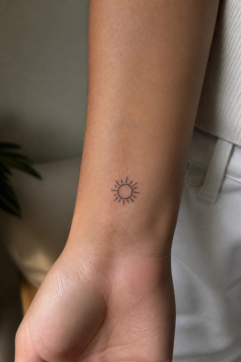 Small black sun tattoo on inner wrist of light-skinned arm with fist