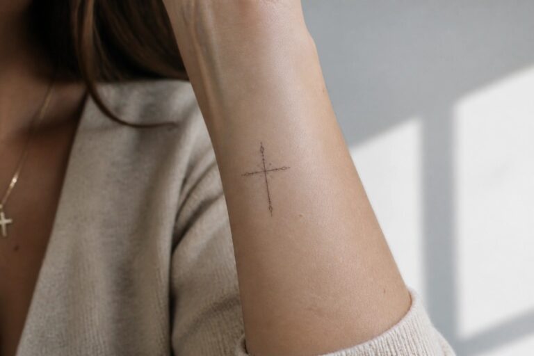 20 Modern Fine Line Christian Tattoos Using Elegant Biblical Symbols Fine line cross tattoo on the inner forearm with dotted lines, small stars, and leaf accents at the ends
