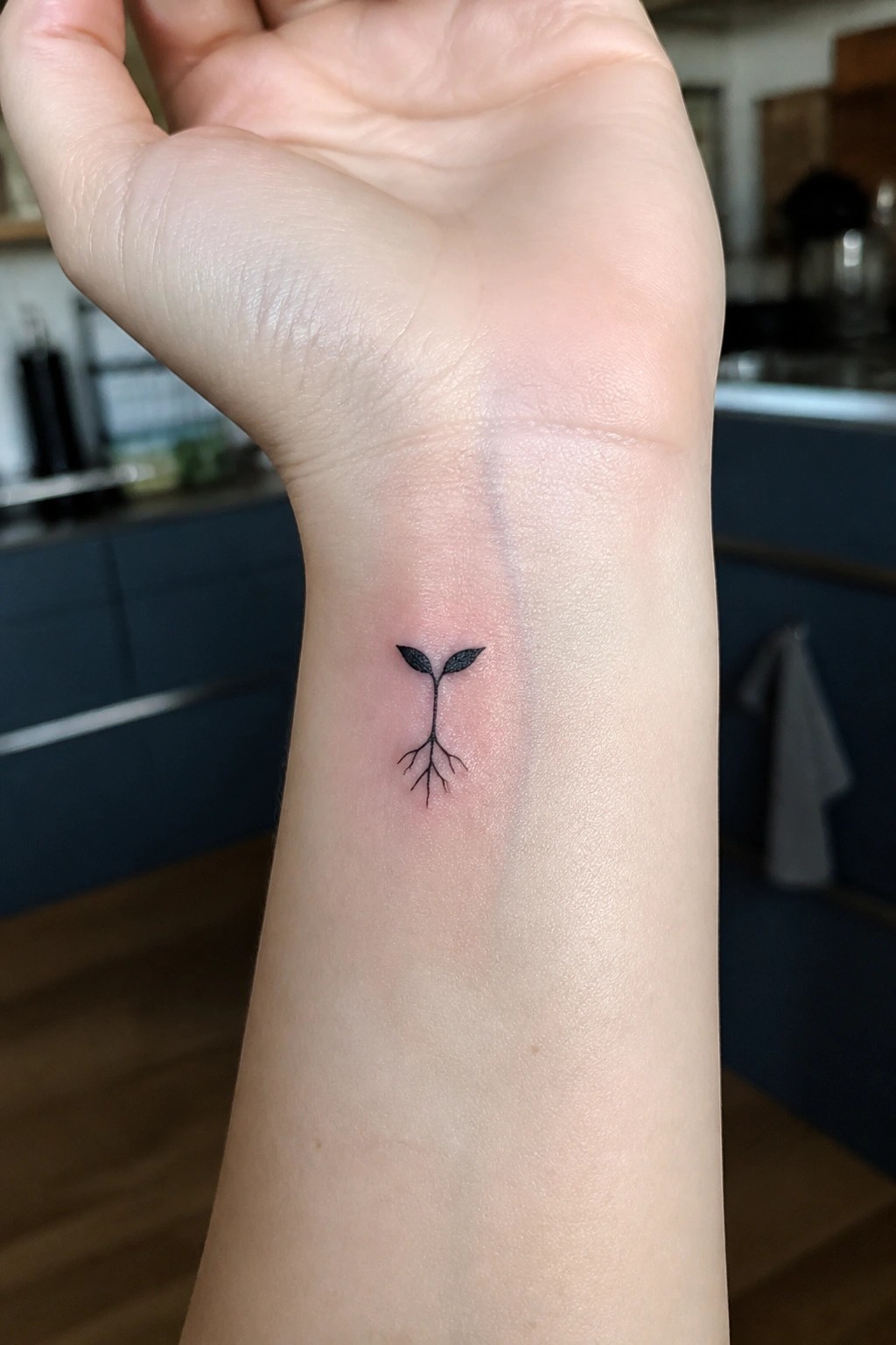 Small black seedling tattoo with leaves and roots on inner wrist