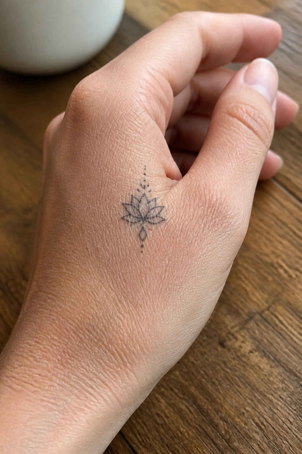 Hand with delicate black lotus tattoo on wooden surface