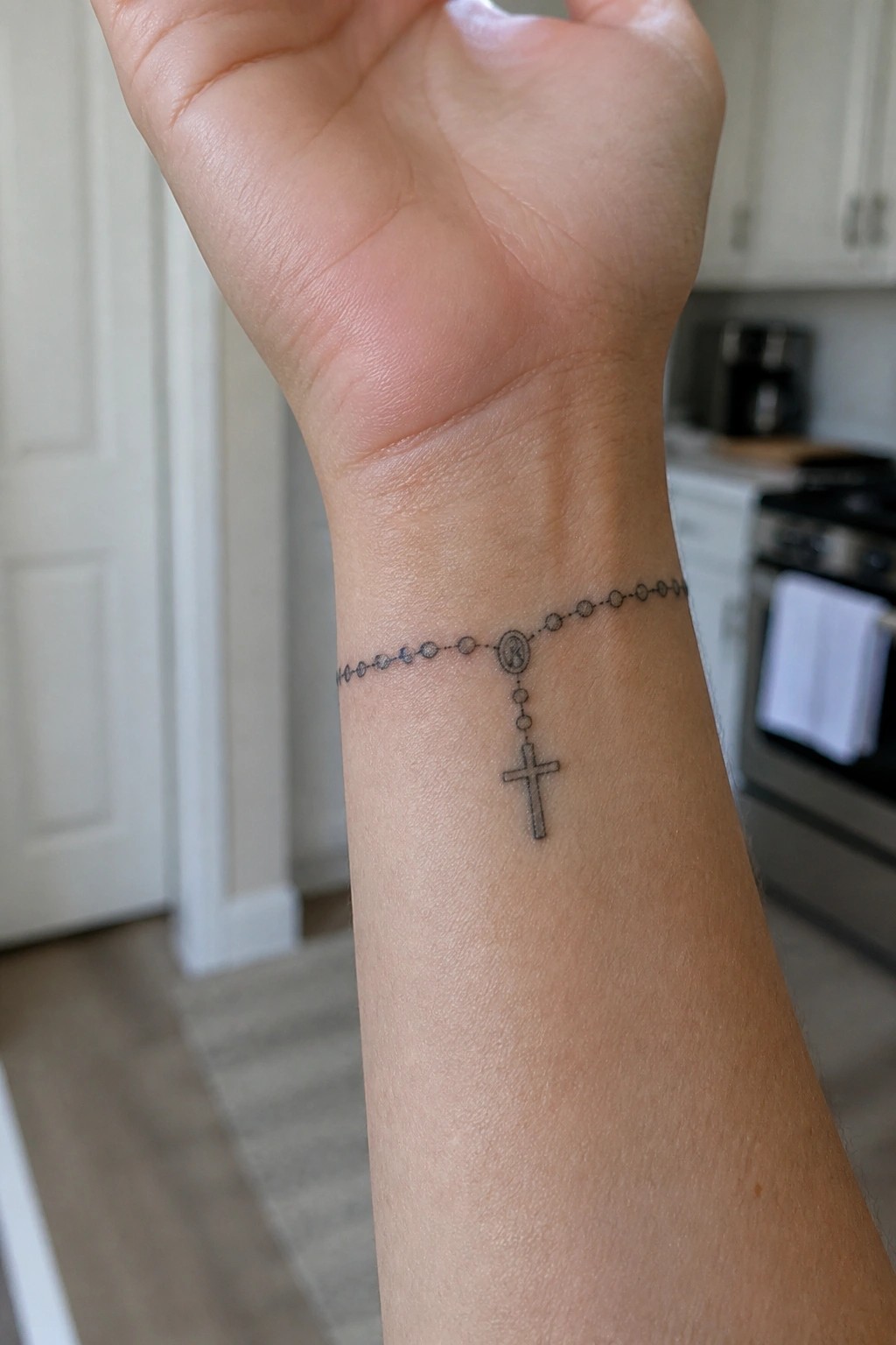 Rosary bead tattoo with cross and medallion on person's wrist.