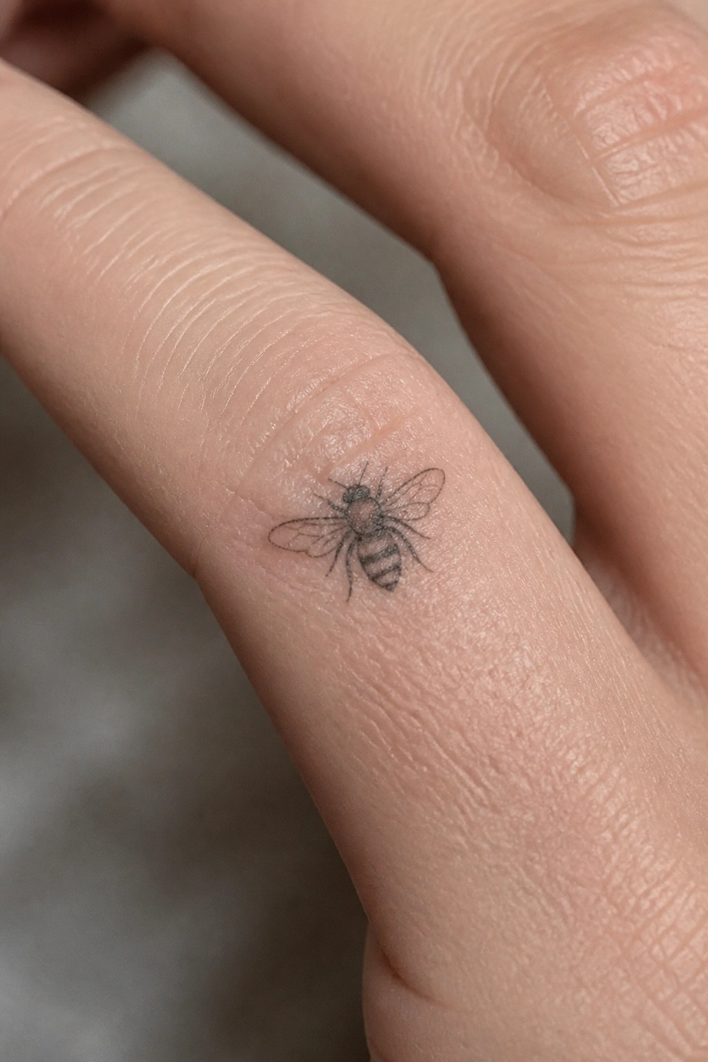 Small black ink bee tattoo on the side of a finger in fine line style
