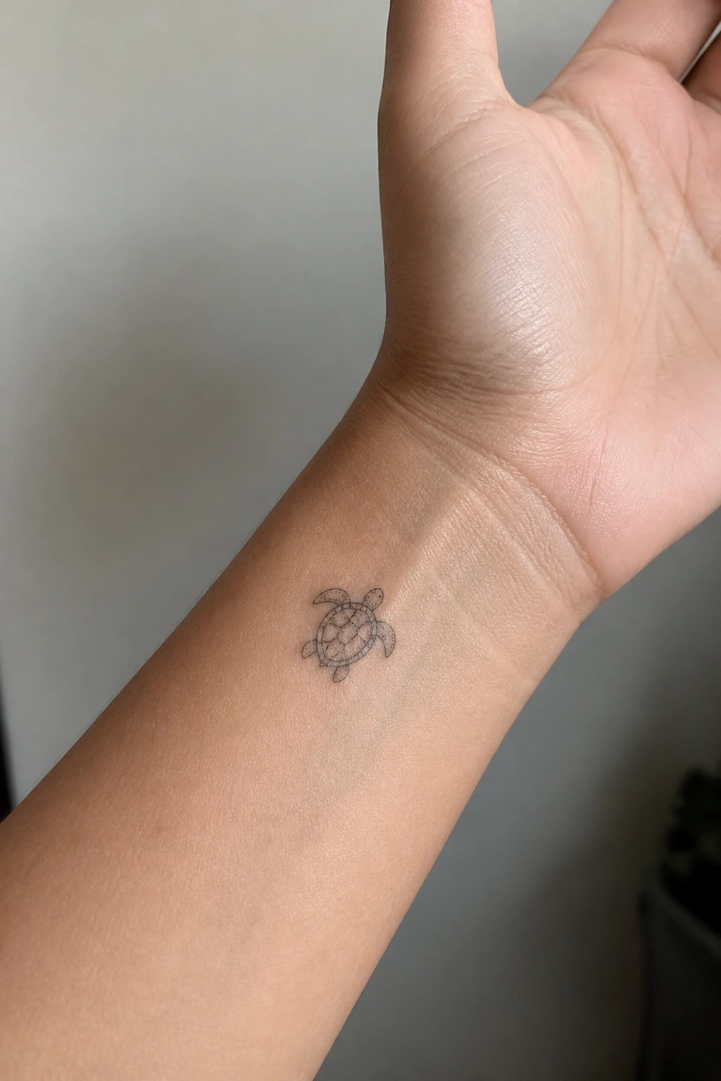 Small sea turtle tattoo on inner wrist of raised light-skinned hand.