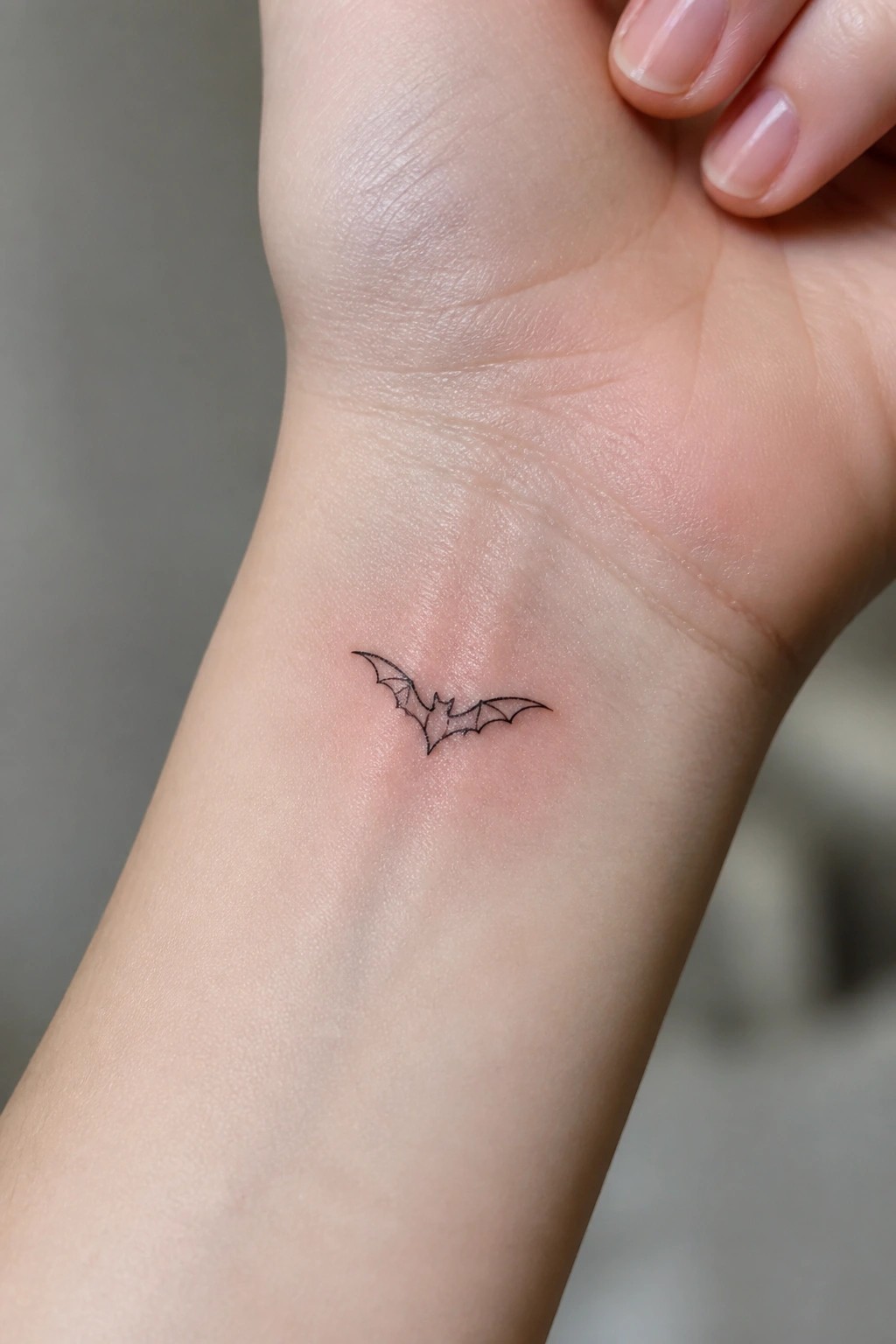 Minimalist fine line bat tattoo on the inner wrist showing a small flying bat outline in black ink.