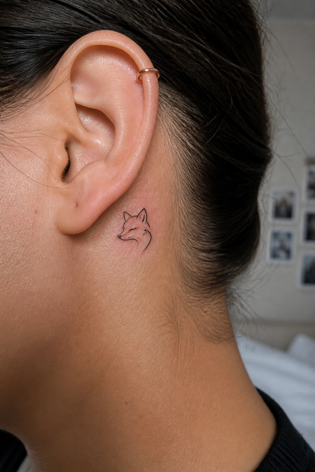 Small fox tattoo behind ear with gold hoop earring in dark hair