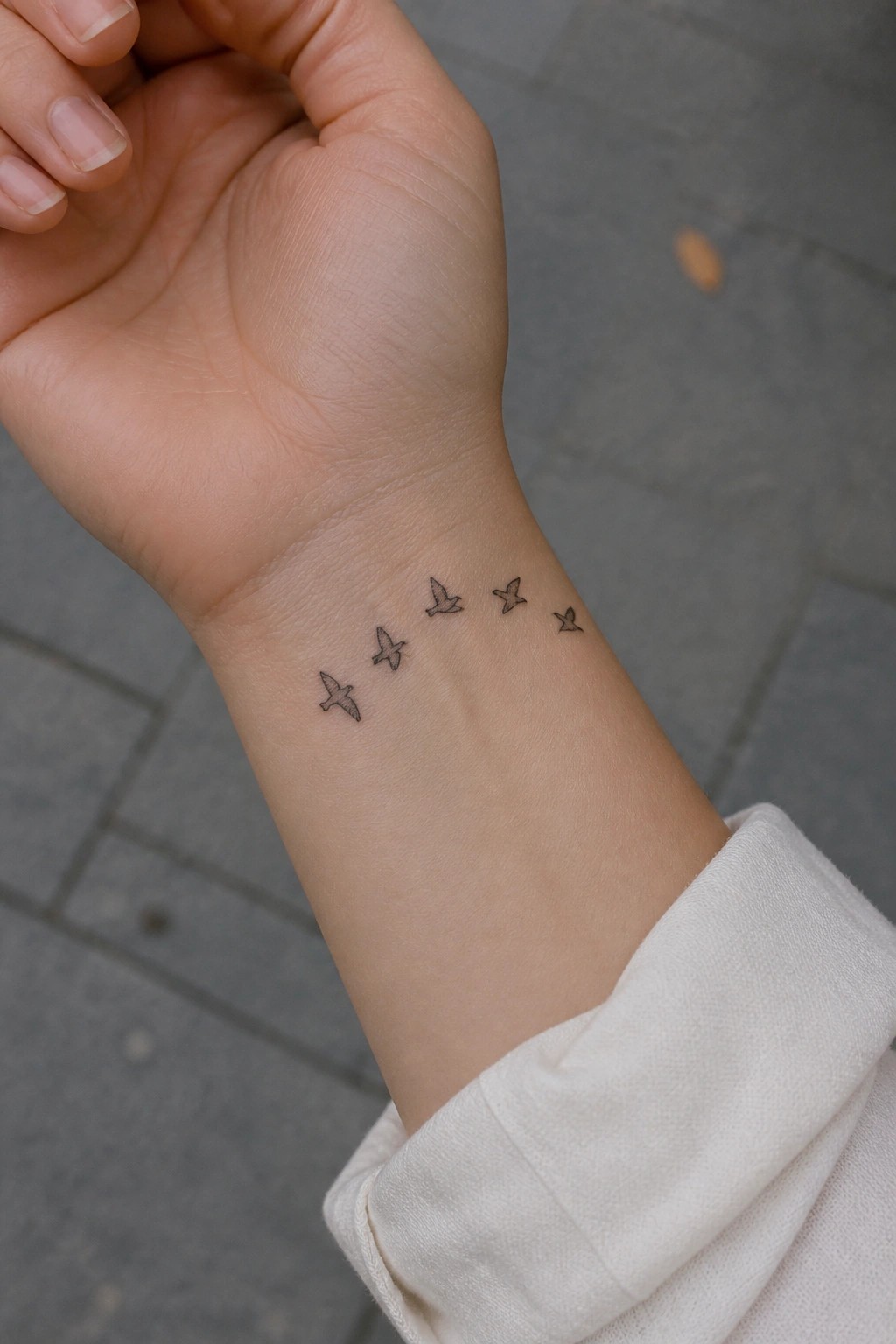Wrist with five small flying bird tattoos above white sleeve cuff