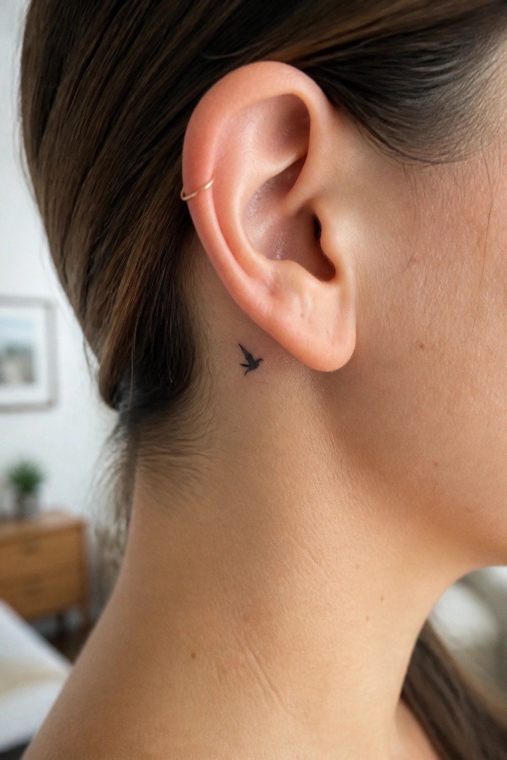 Small black bird tattoo behind ear beside thin gold hoop earring