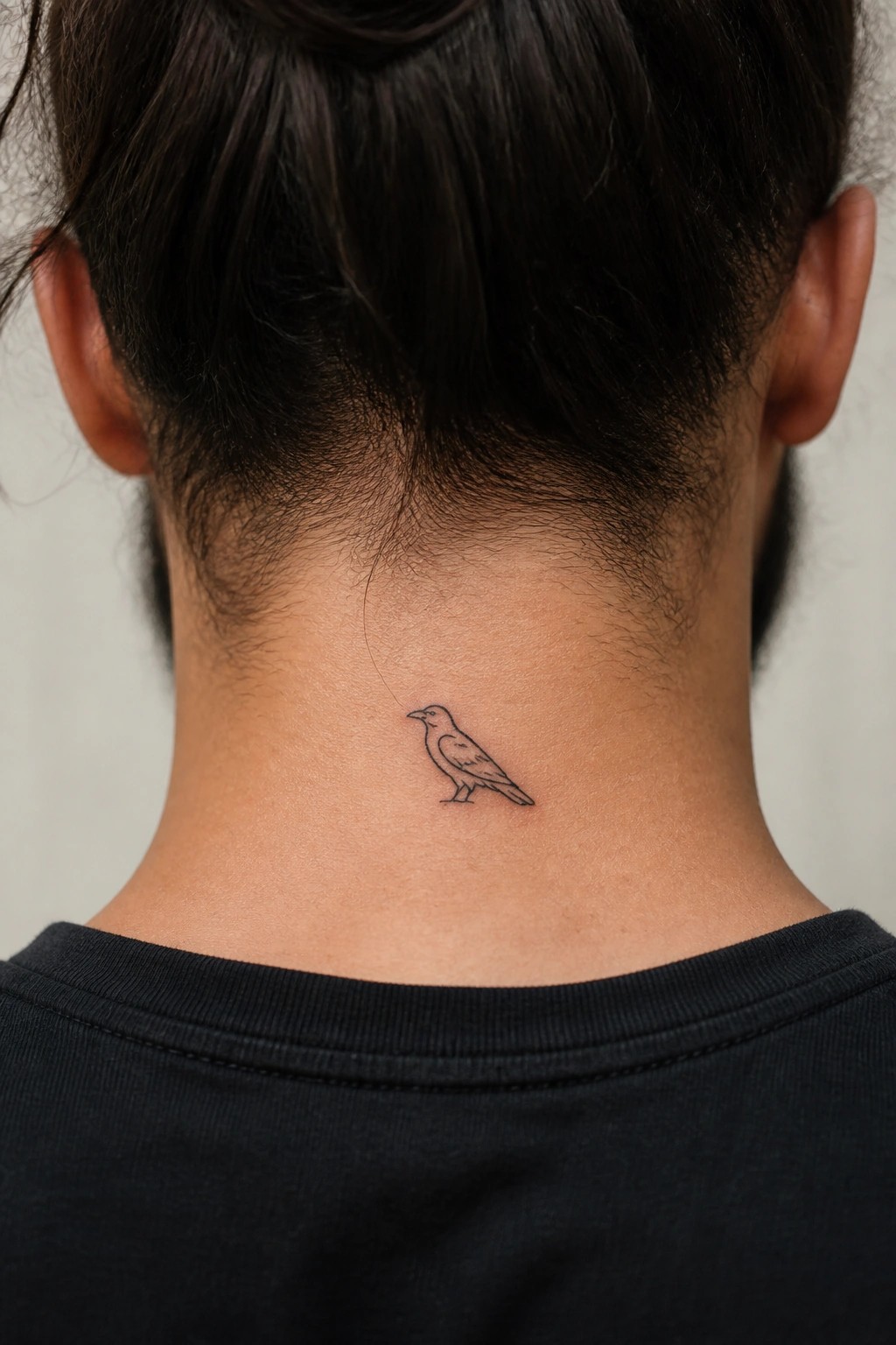 Fine line bird tattoo on the back of the neck just below the hairline