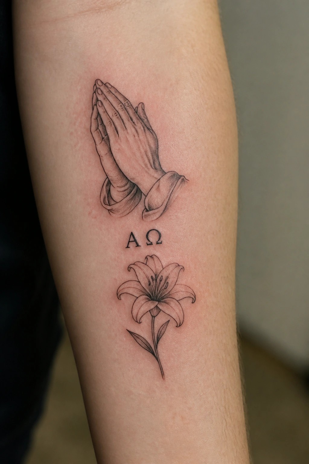 Black ink forearm tattoo of praying hands above A Ω and lily flower.