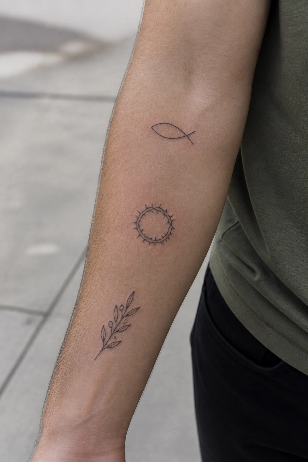 three small christian symbols in fine lines spaced vertically on the inner forearm including a fish, crown of thorns, and leafy branch