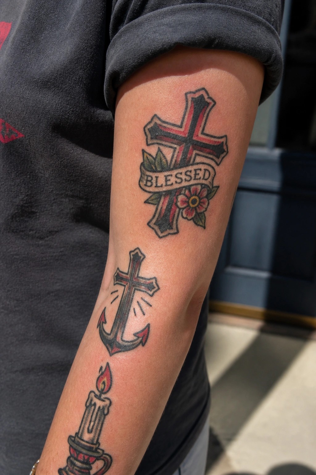 Arm showing three traditional Christian tattoos with a blessed cross at the top, an anchor cross in the middle, and a lit candle at the bottom.