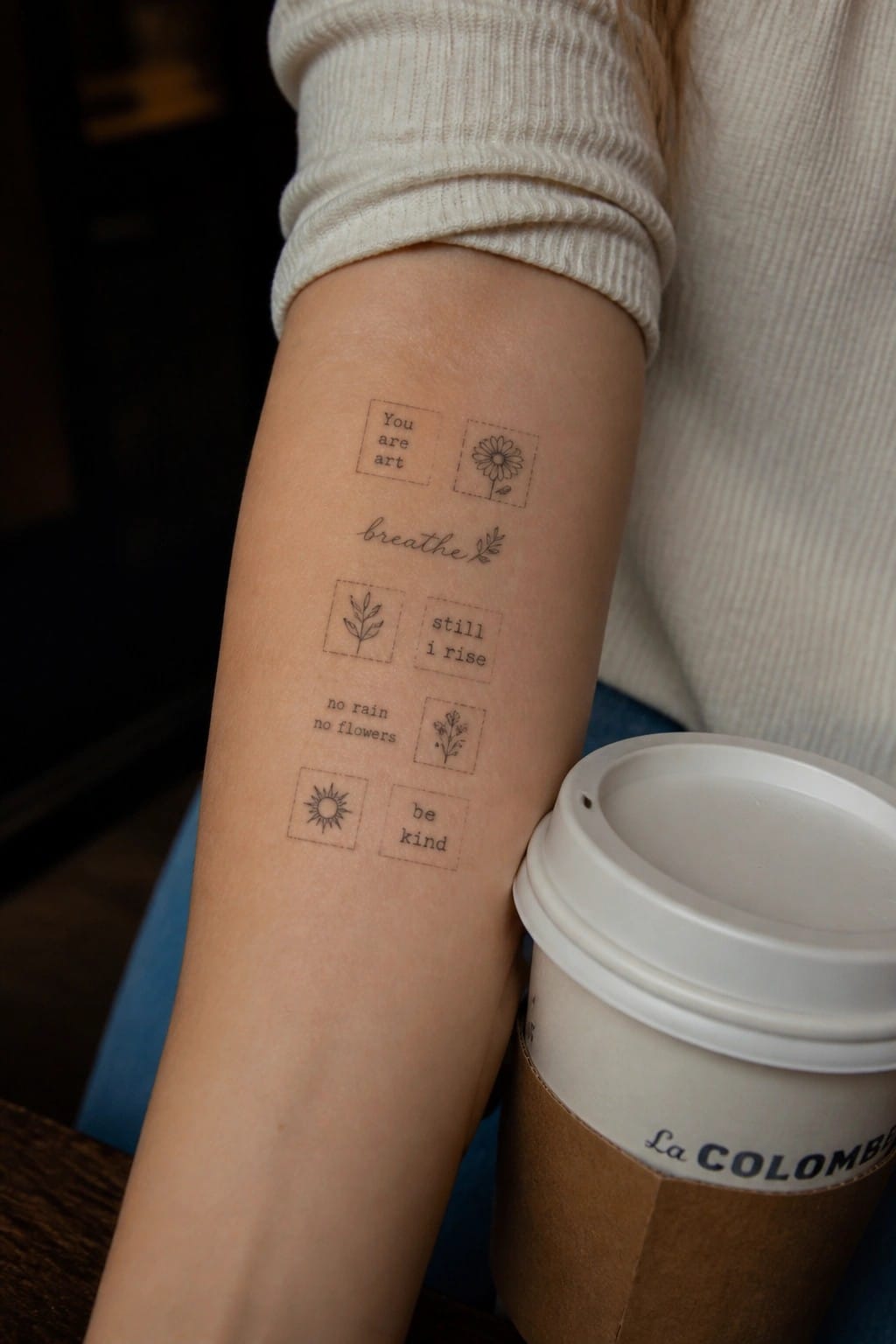 Arm in cream sweater with small quote tattoos beside La Colombe coffee cup