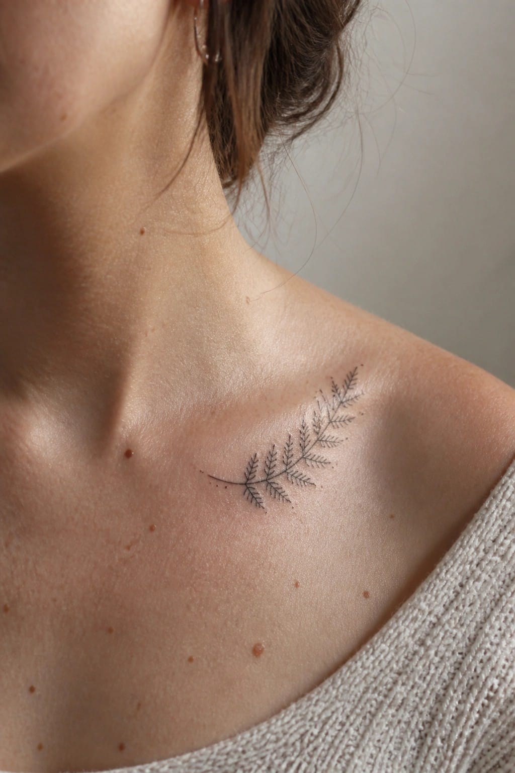 Delicate black fern tattoo on freckled shoulder above light knit sweater