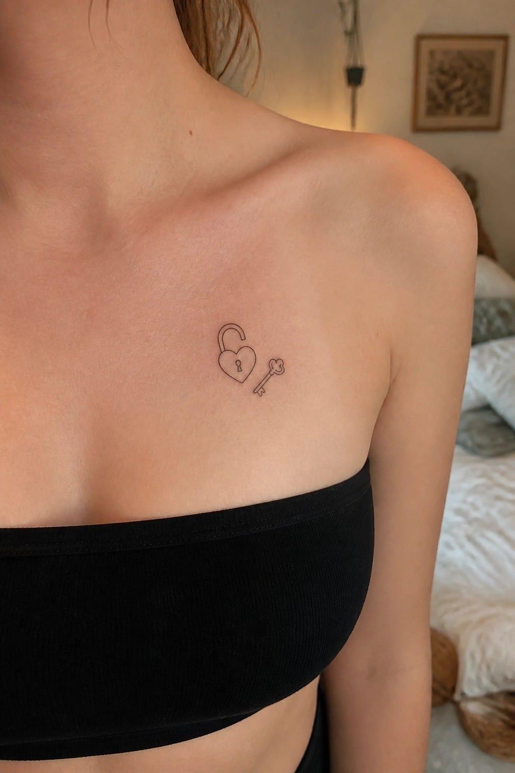 Heart-shaped padlock and key tattoo on chest above black strapless top in bedroom