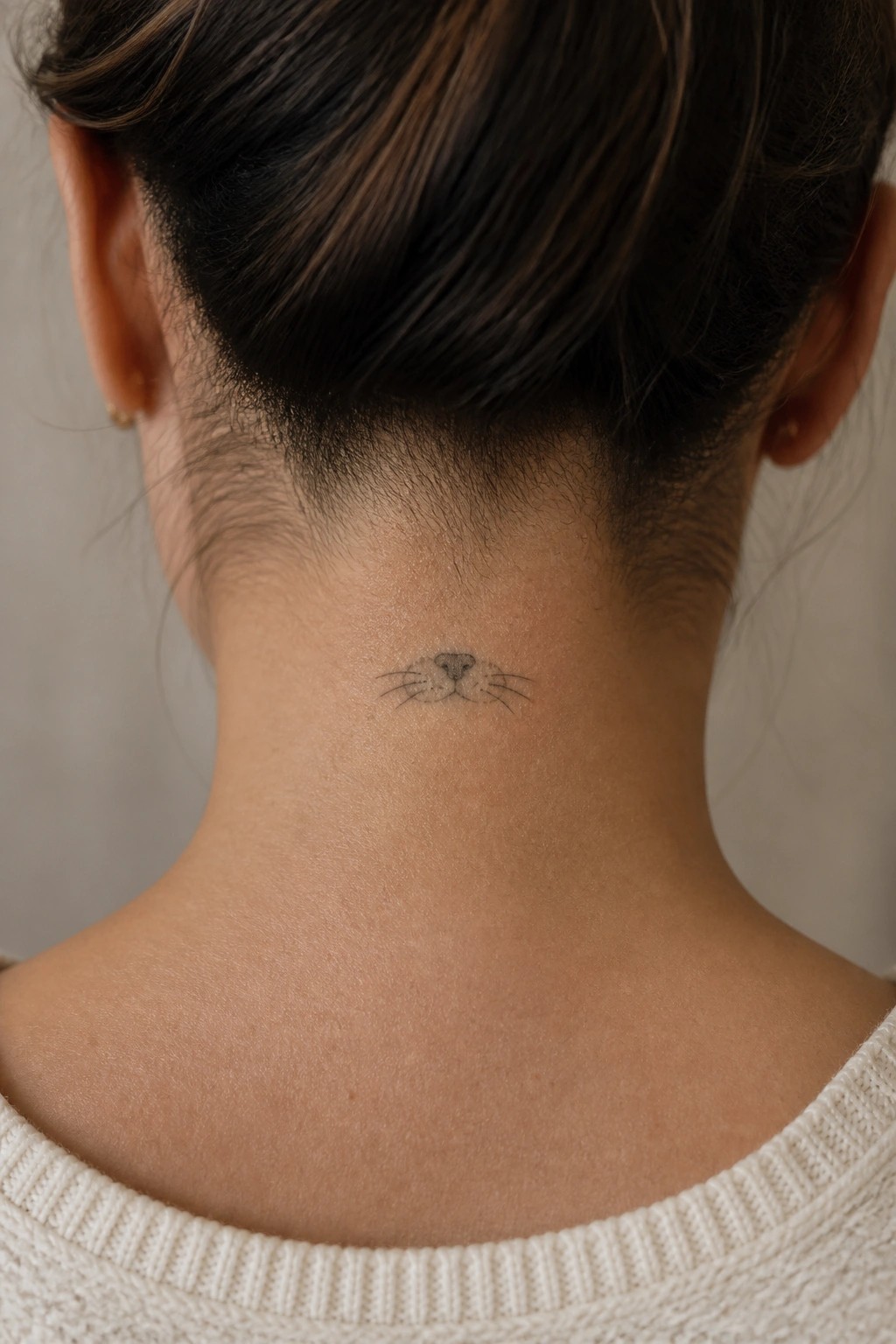Minimal otter nose and whiskers tattoo centered on the back of the neck in fine black lines