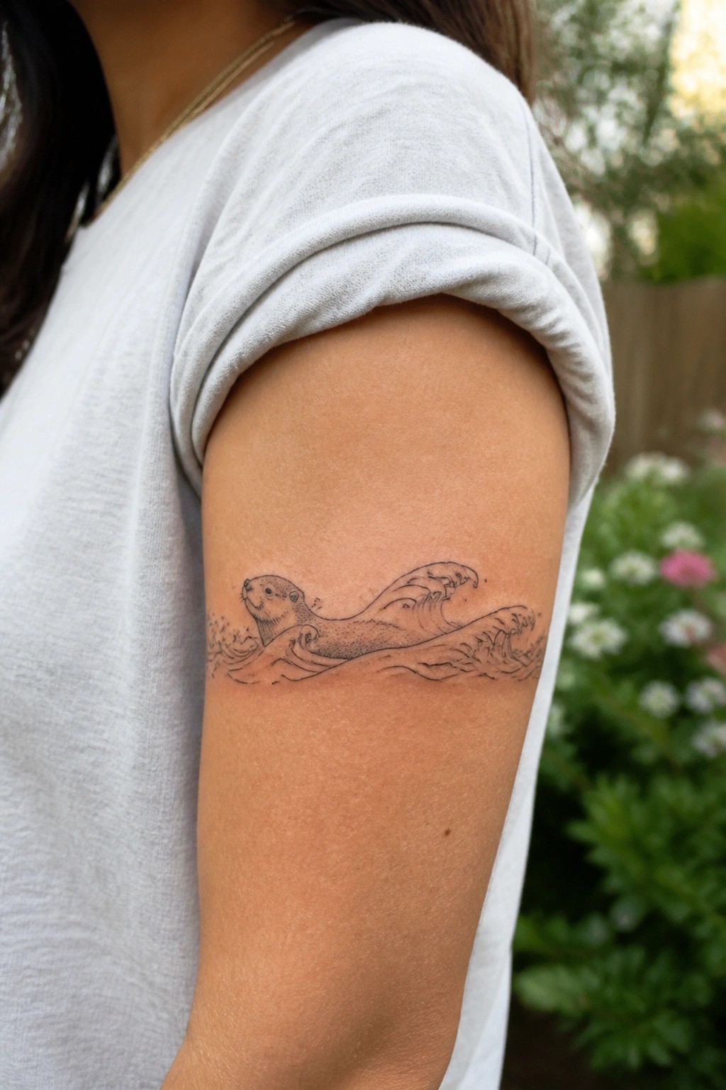 Otter swimming in waves tattoo on upper arm under white t-shirt sleeve