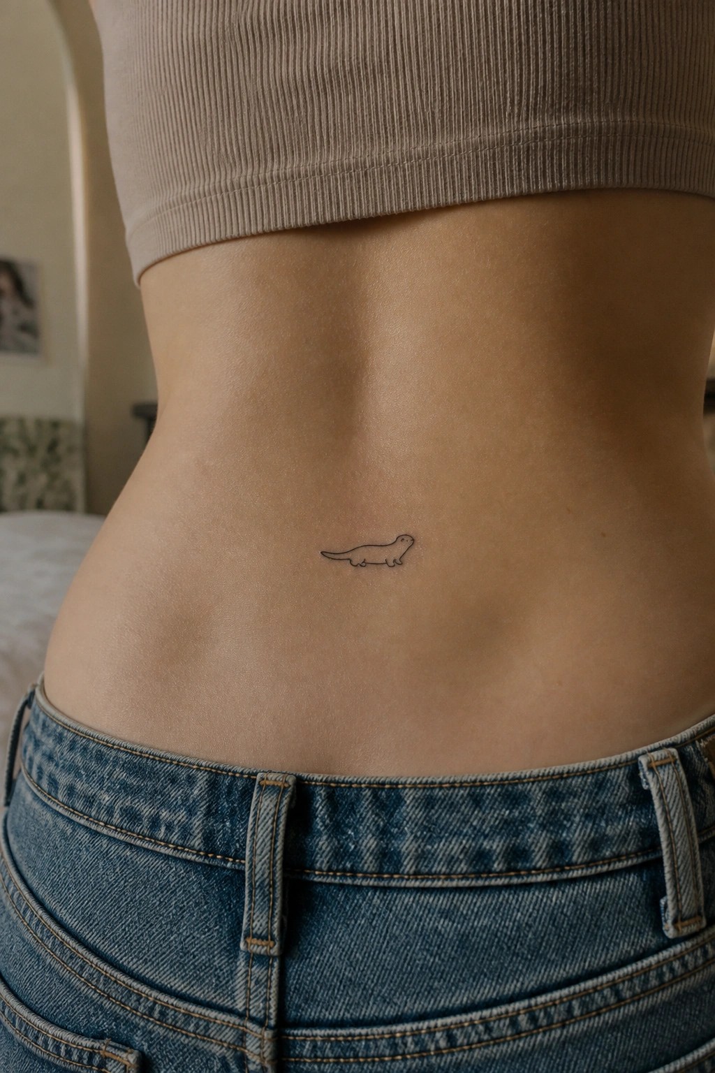 Small otter tattoo on midriff above blue jeans and below beige crop top.