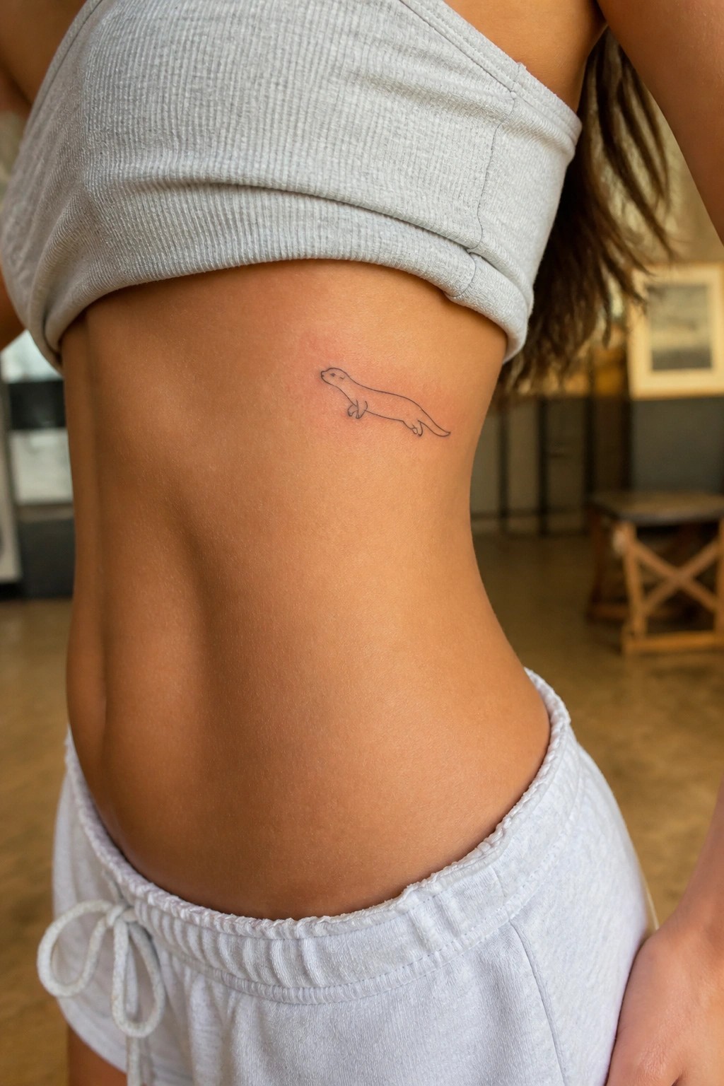 Otter tattoo on midriff under lifted gray crop top and white drawstring shorts