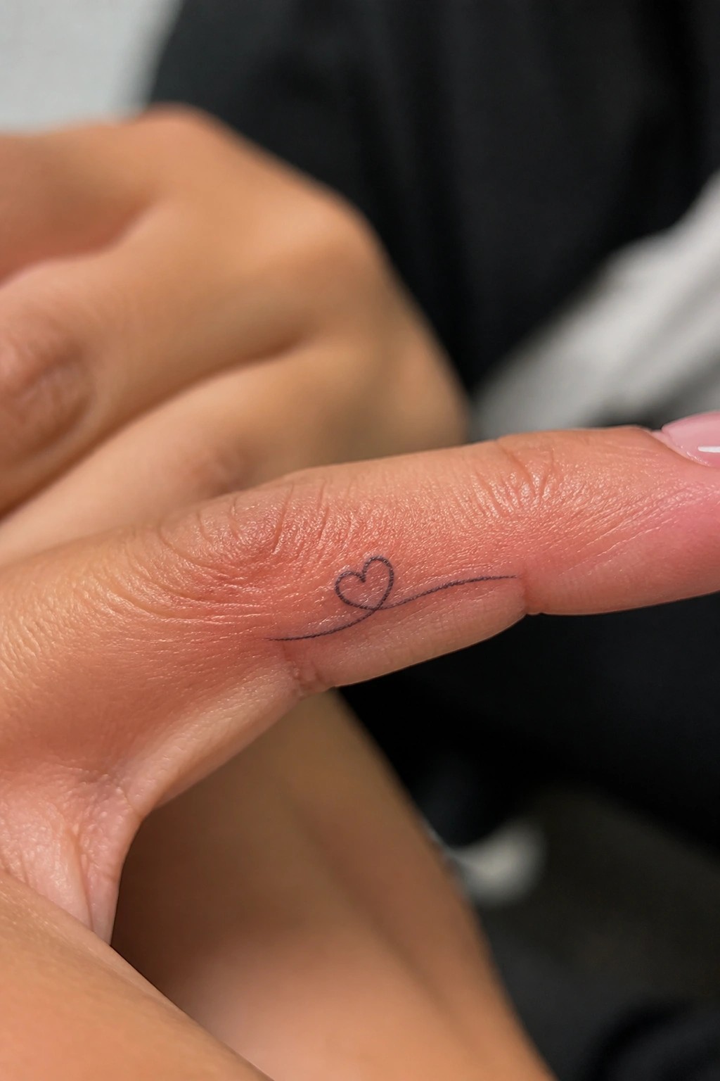 Finger with small black heart tattoo and thin extending line on red skin