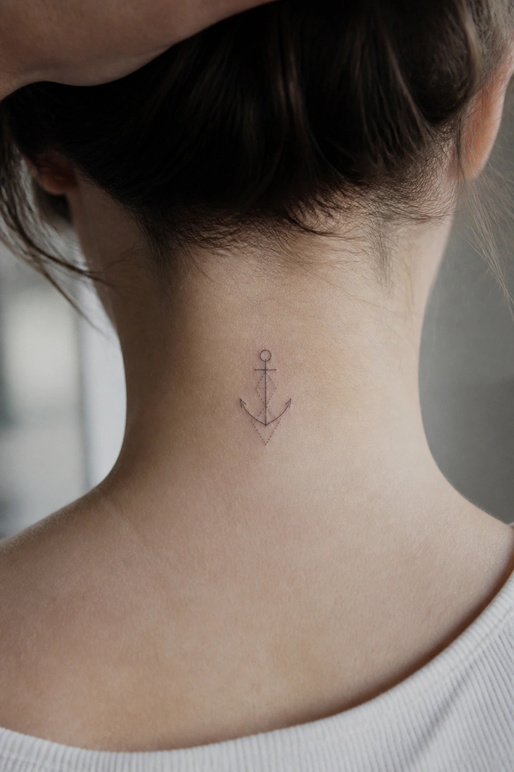 Small black anchor tattoo on nape of neck below dark hair in bun
