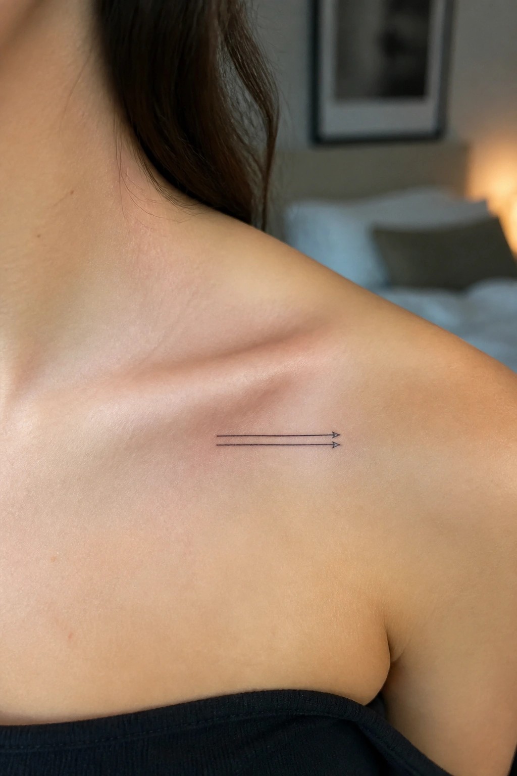 Small two-line arrow tattoo on bare shoulder with dark hair and black top