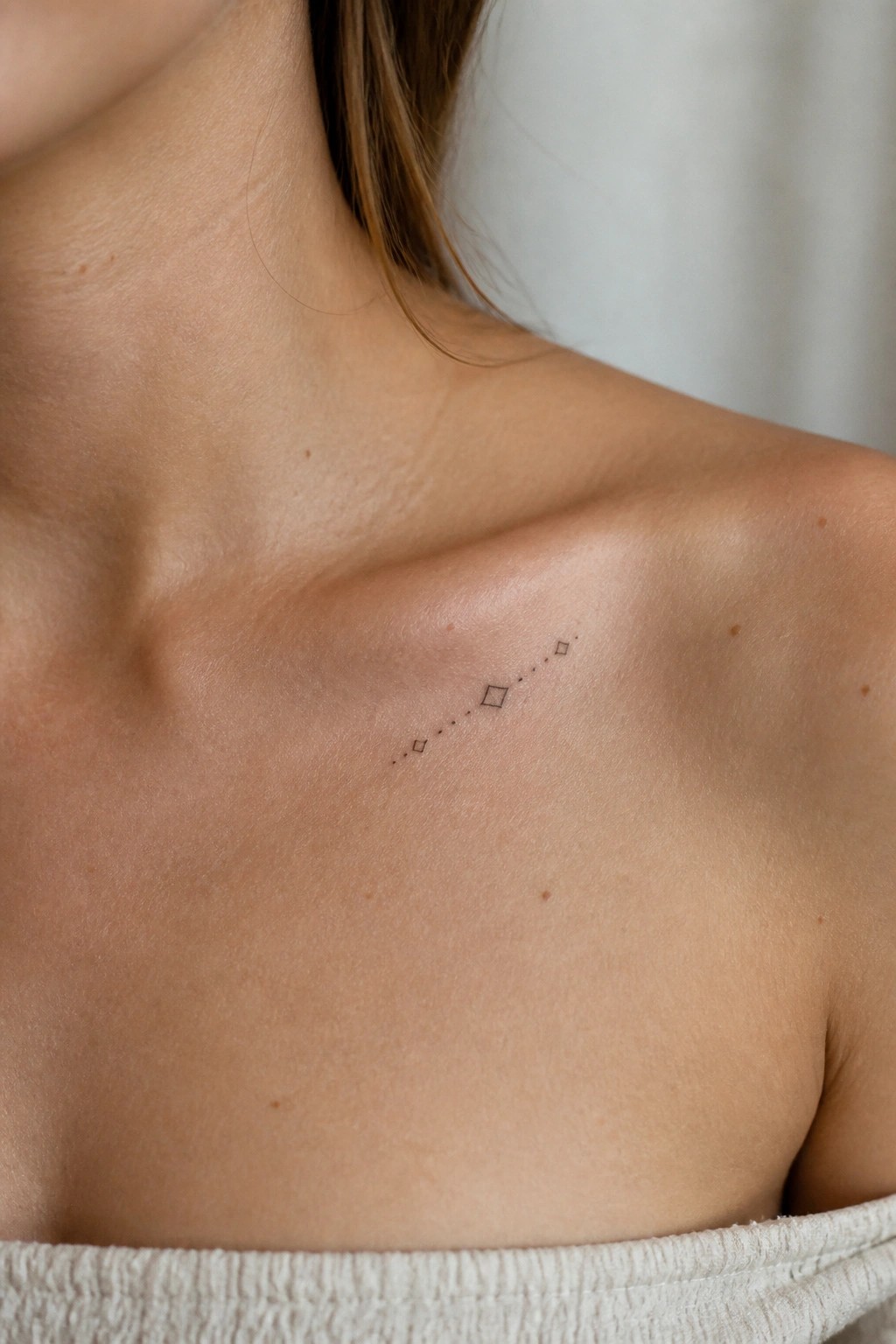 Fine line minimalist tattoo of connected diamonds placed diagonally on the collarbone