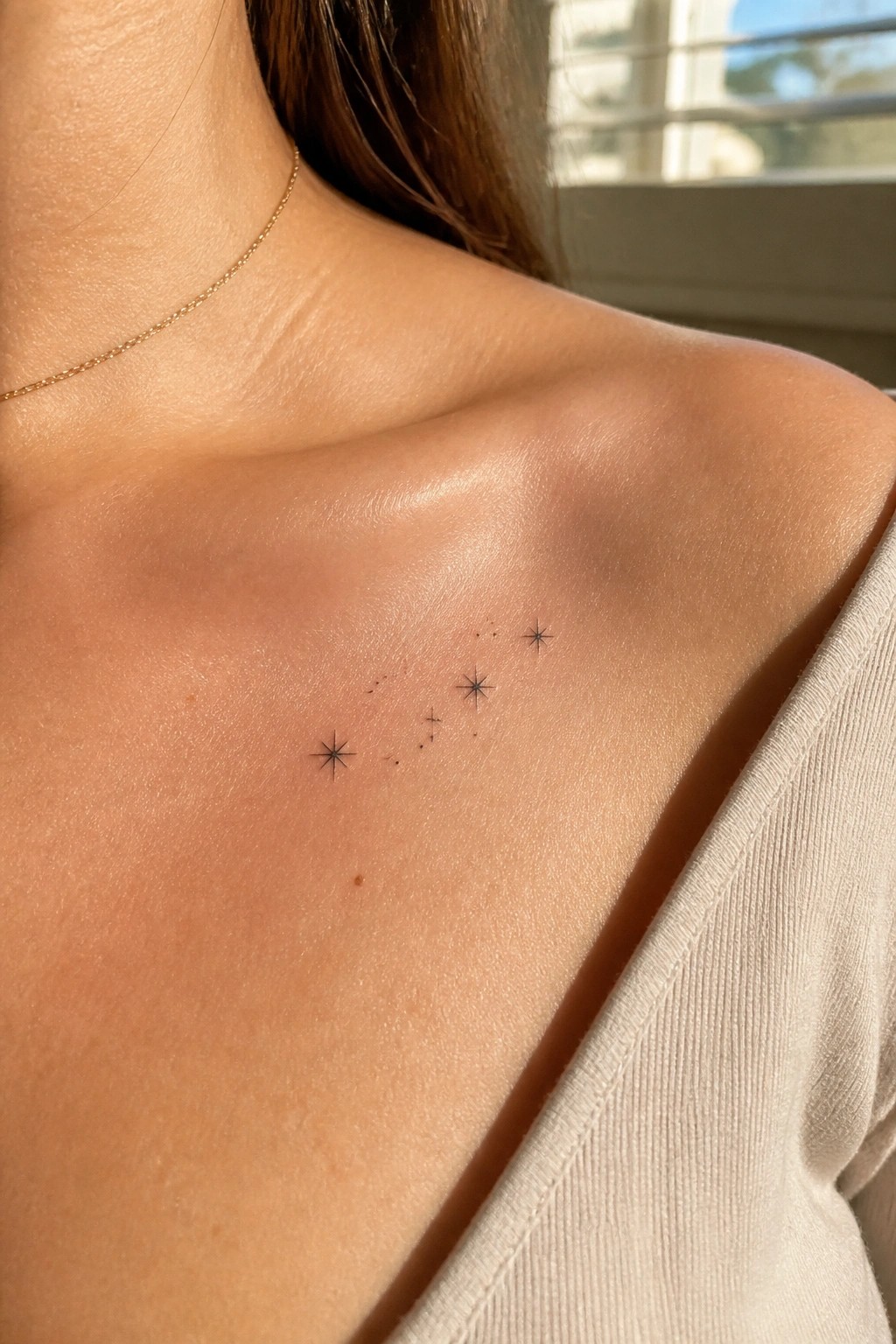 Shoulder with black star constellation tattoo, gold necklace, and light top.
