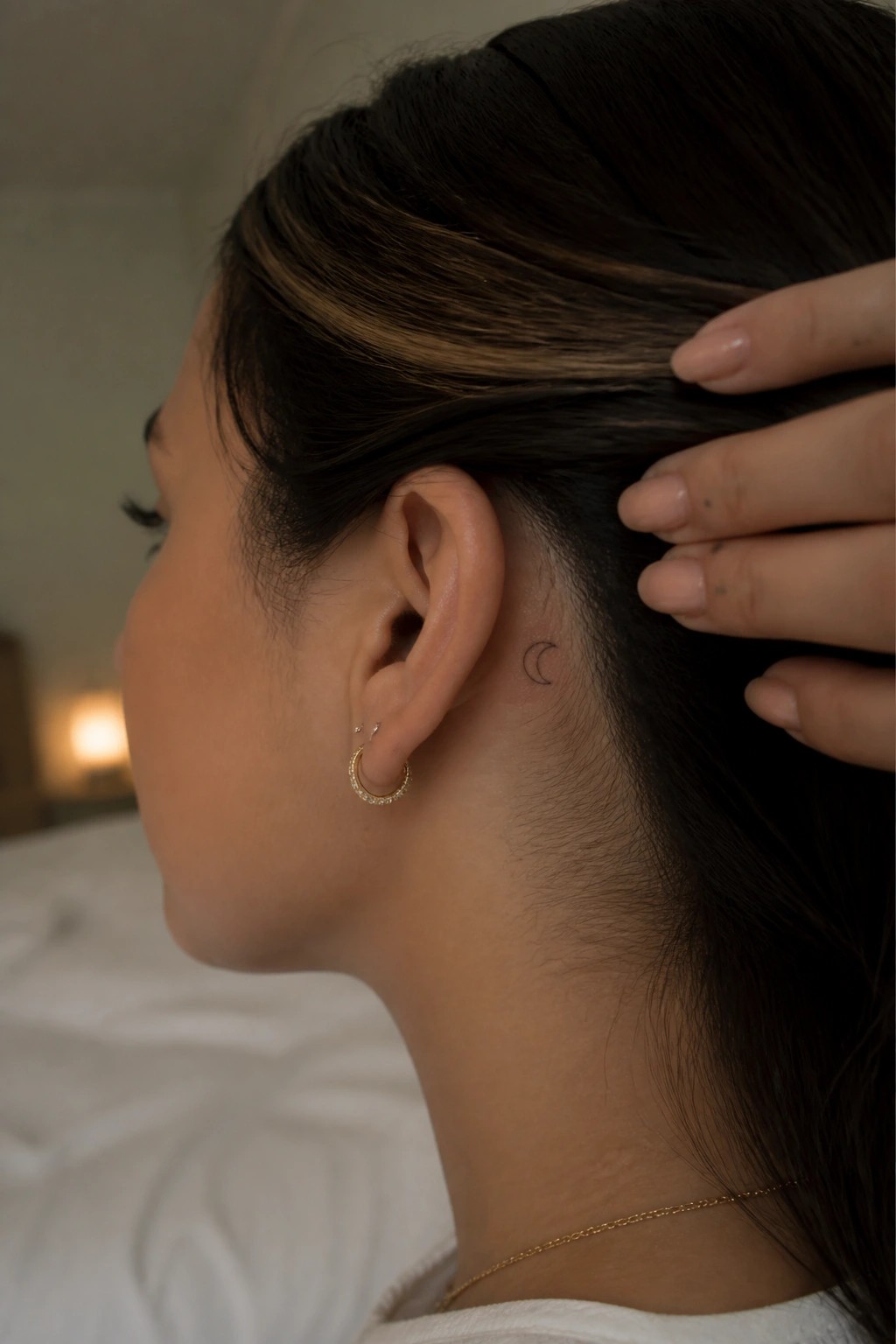 Woman's profile with crescent moon tattoo behind ear and gold hoop earrings