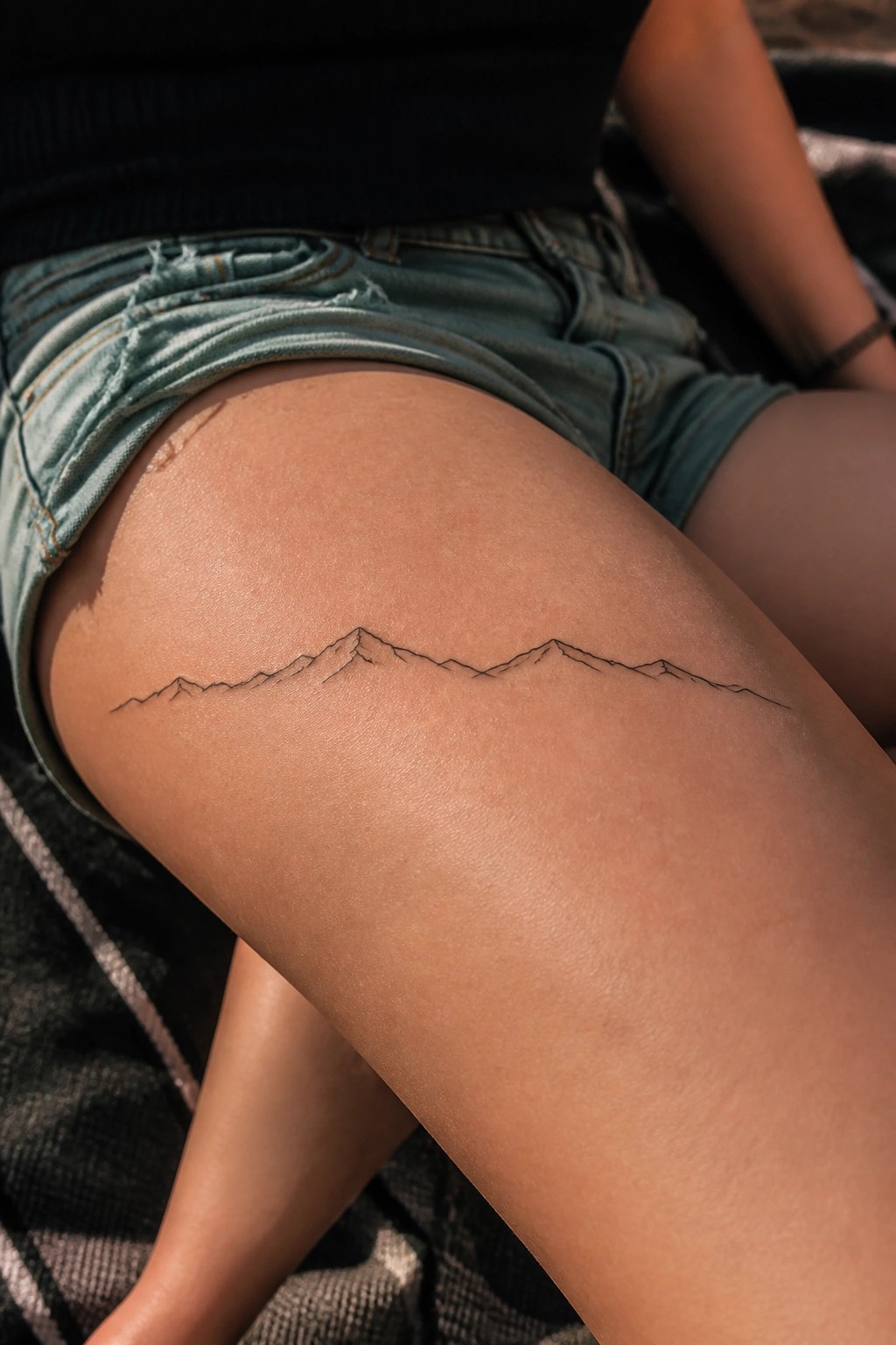 Minimalist black line tattoo of mountain peaks across the upper thigh