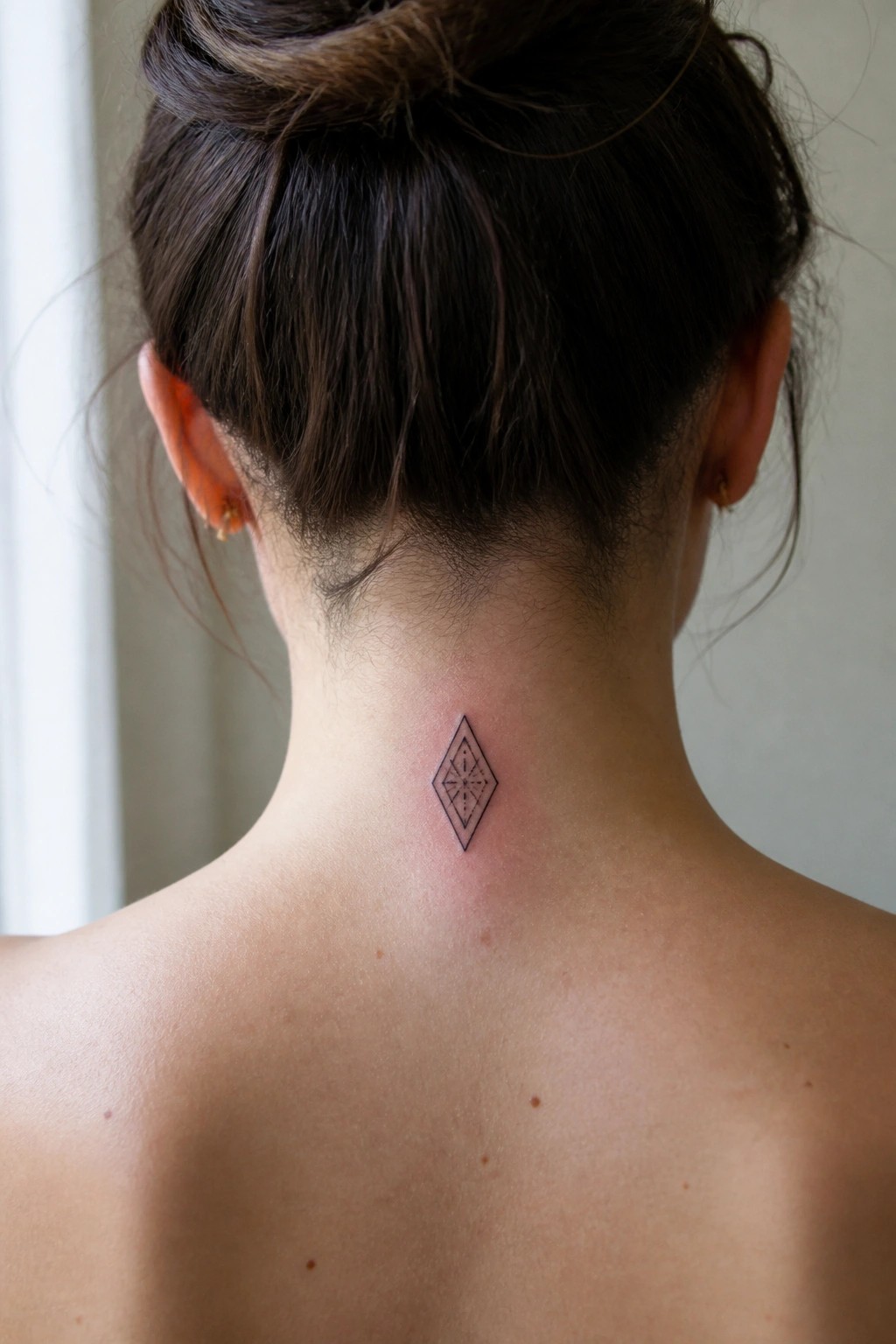 Back of neck with geometric diamond tattoo below dark hair in bun