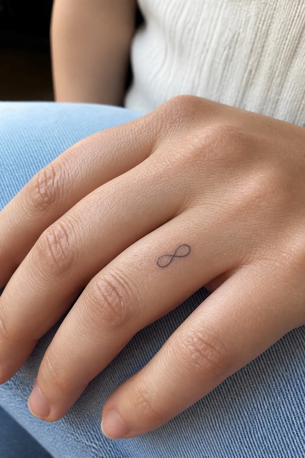 Hand with small infinity tattoo on ring finger resting on blue denim