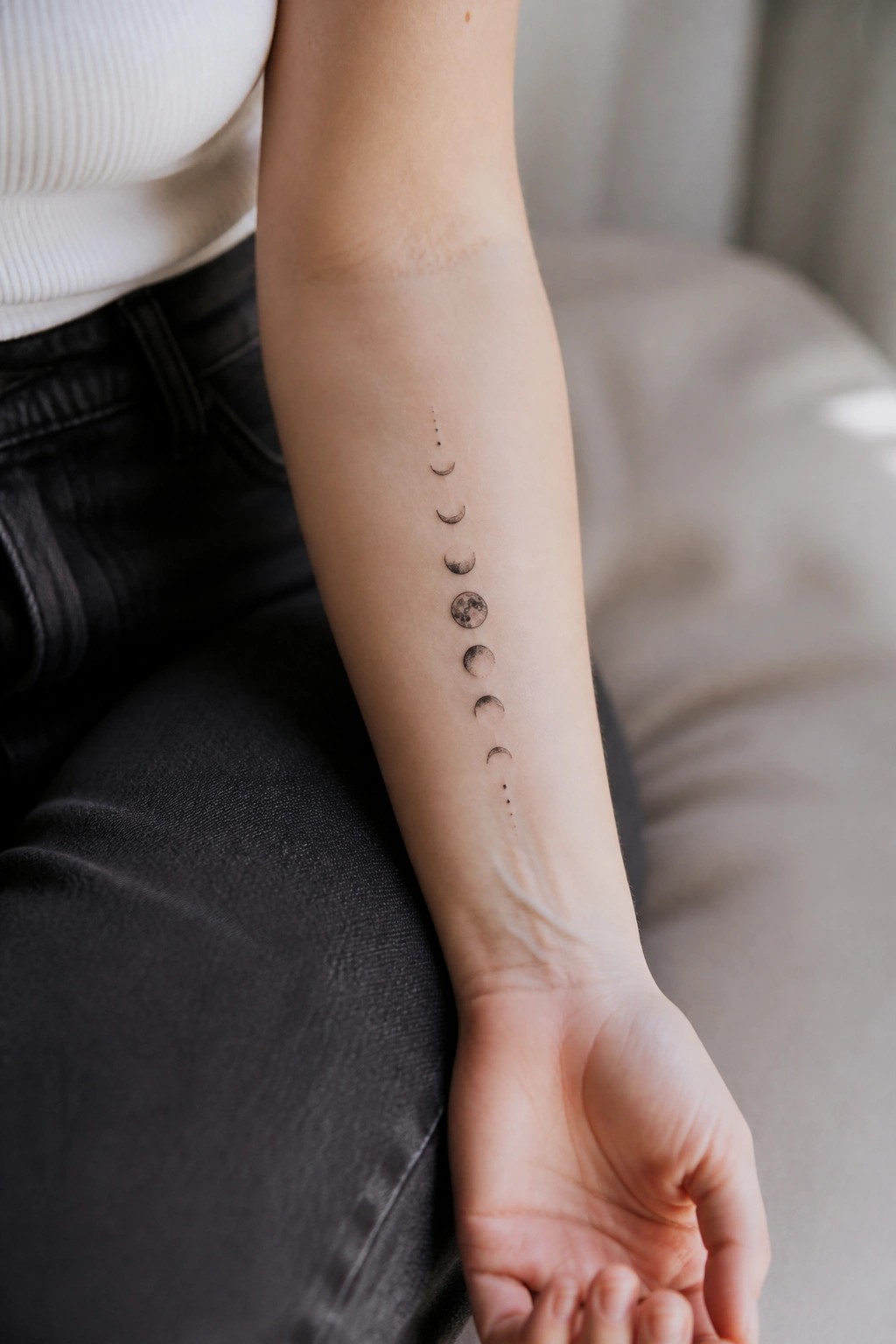 A vertical row of moon phases tattooed in black ink along the inner forearm