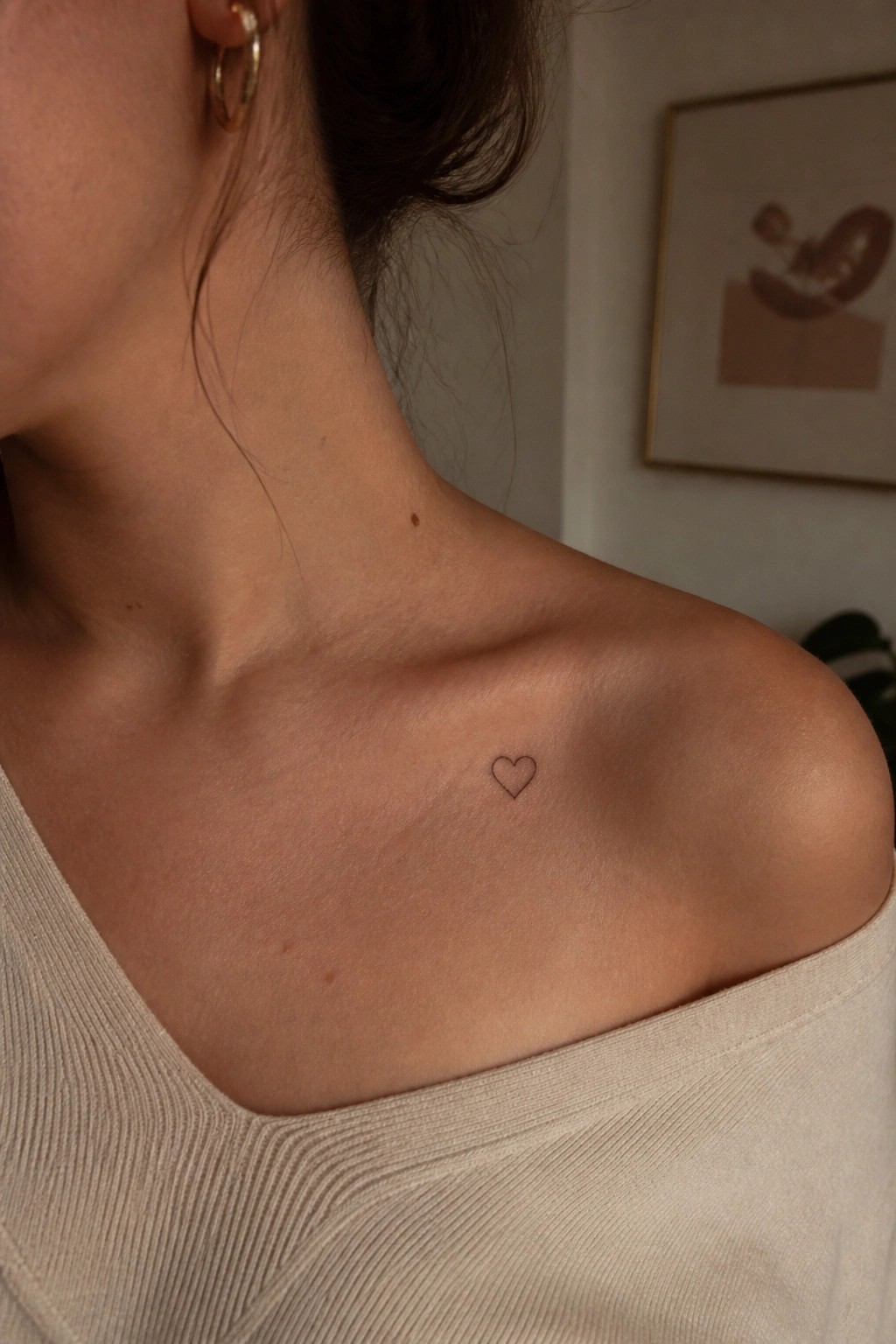 Woman's shoulder with small heart tattoo, wearing beige off-shoulder ribbed top