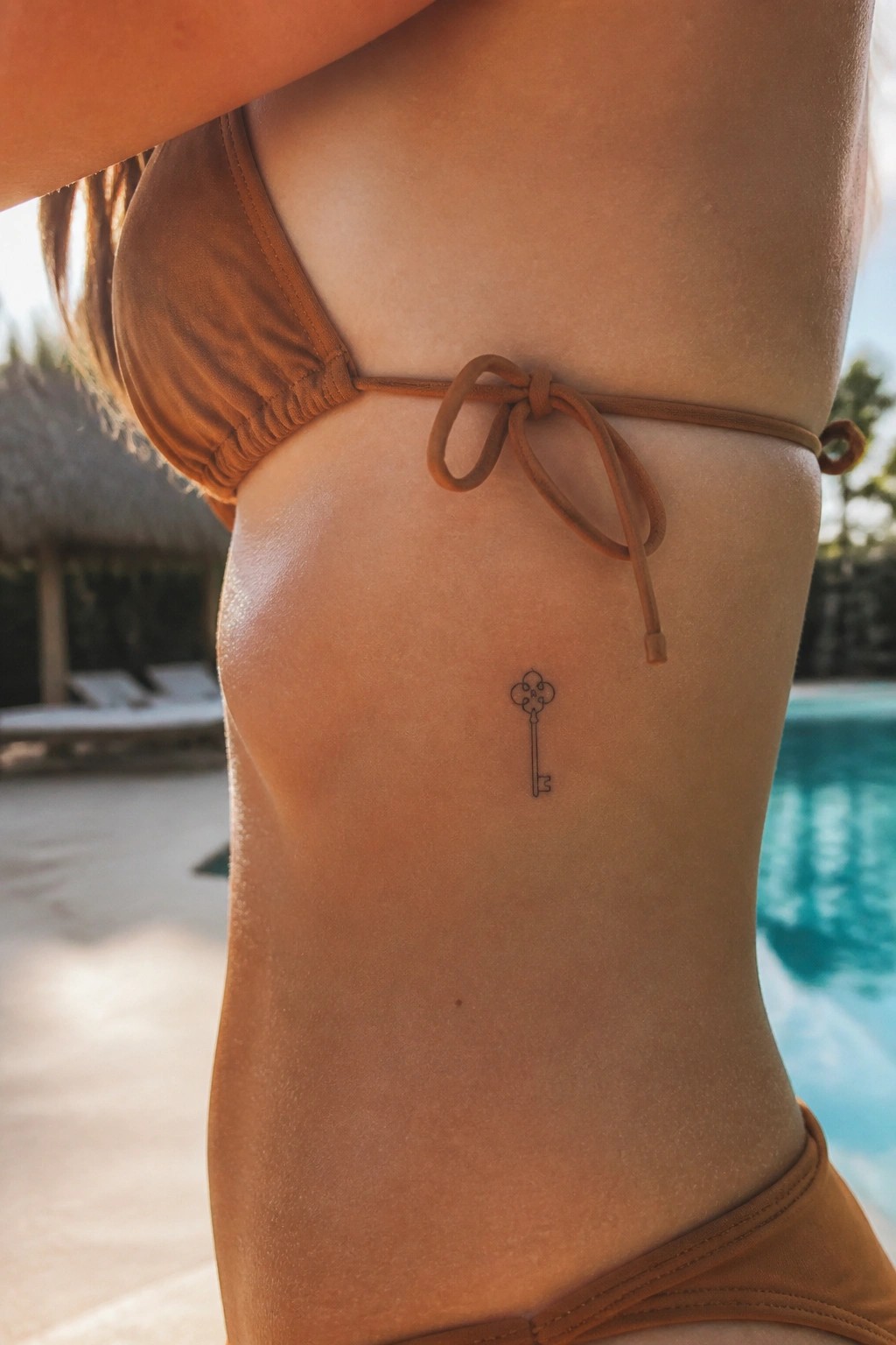 Woman's tanned torso in brown bikini with small key tattoo by pool