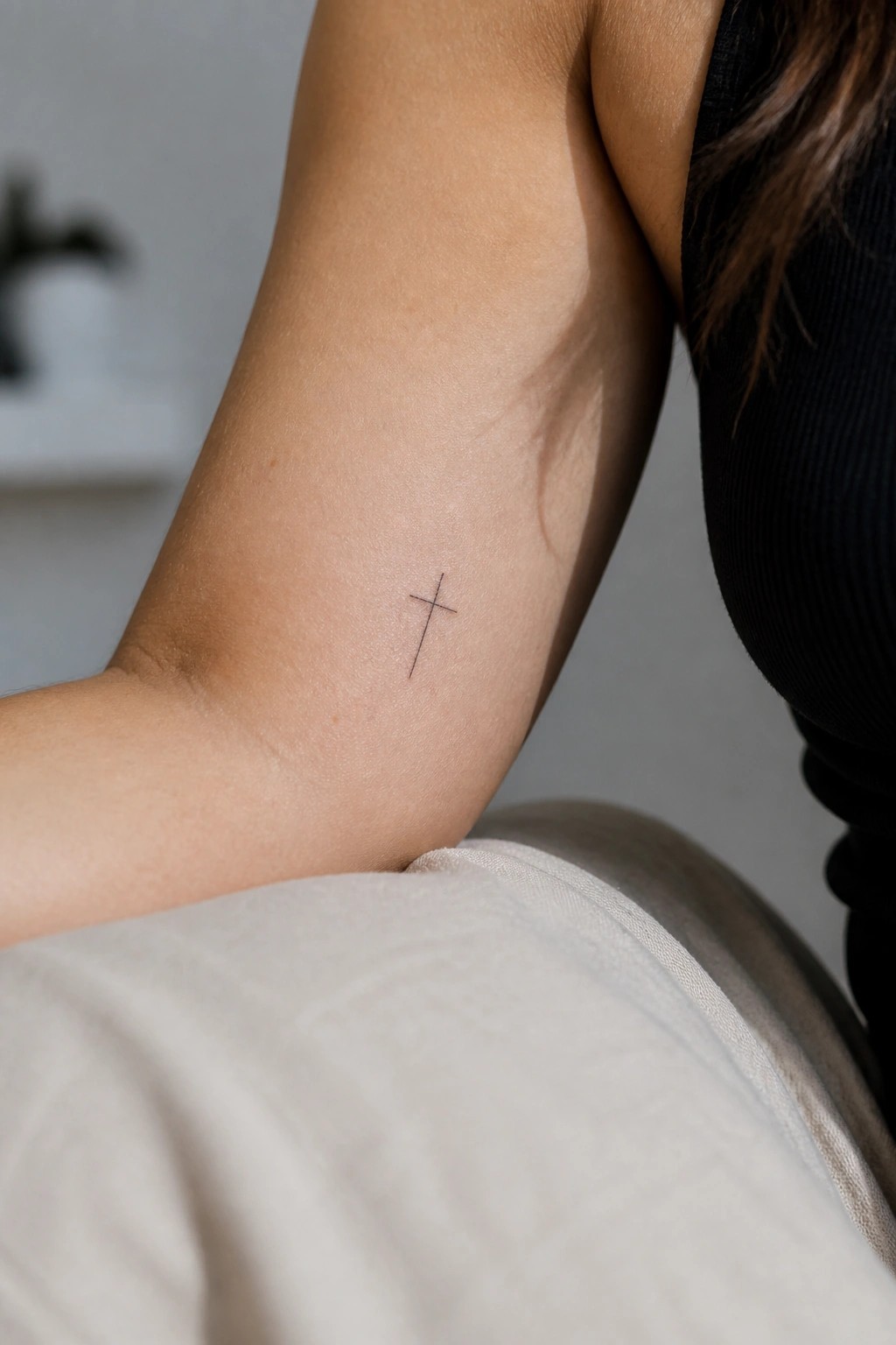 Small cross tattoo on upper arm beside black top and light fabric