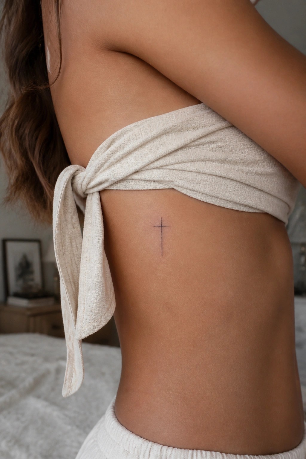 Small cross tattoo on skin beneath beige knotted wrap top on torso.