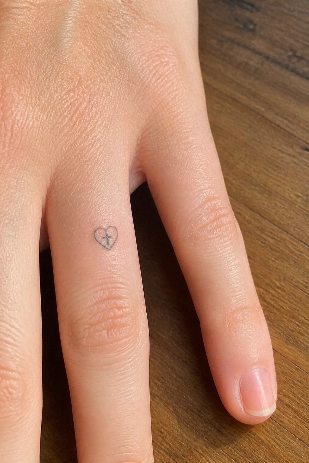 Small heart outline with cross inside on the side of a finger