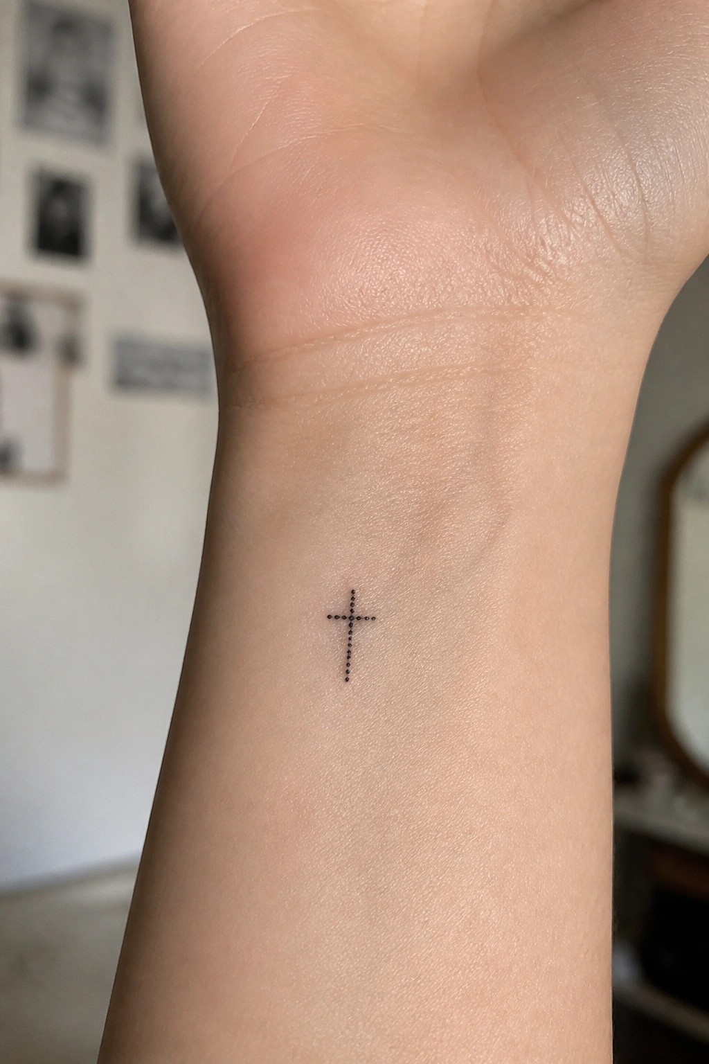 Small dotted cross tattoo centered on a light-skinned inner wrist