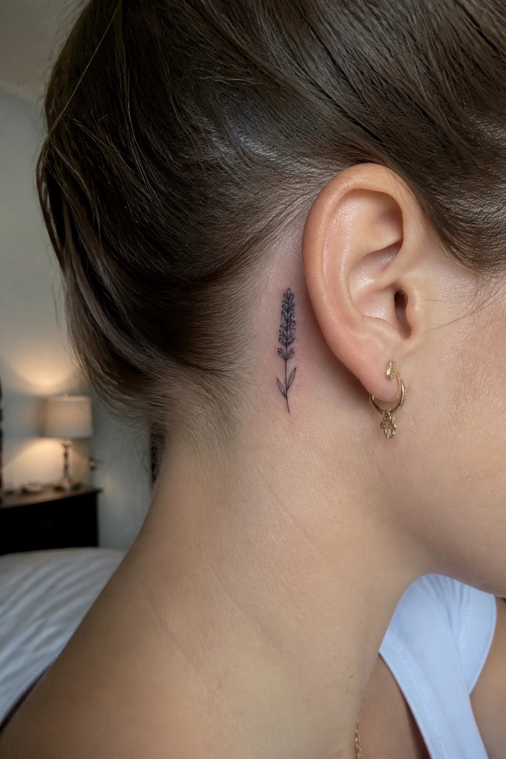 Brown hair pulled back showing small lavender tattoo behind ear with gold hoop earring