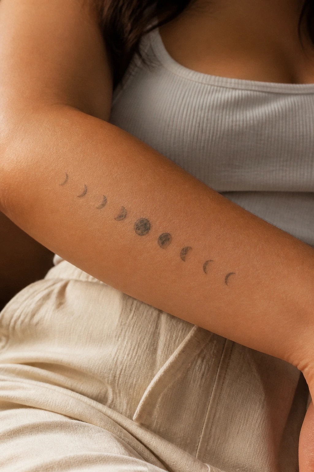 Minimalist moon phases tattoo arranged in a horizontal line on a woman's inner forearm