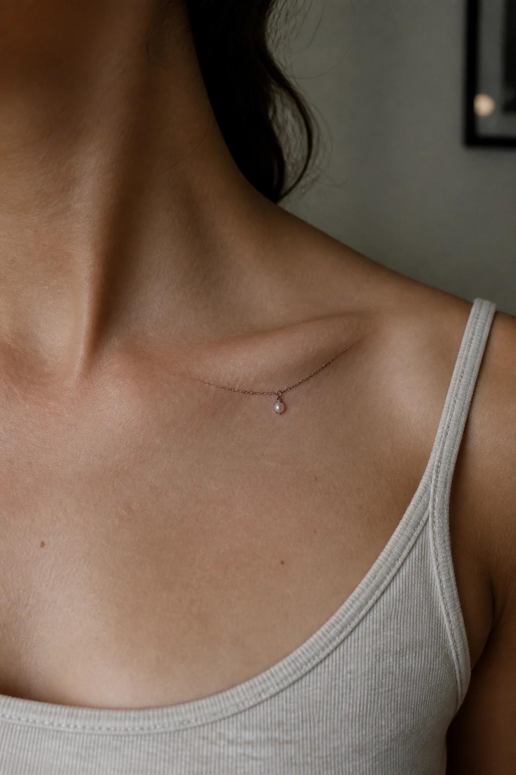 Delicate gold necklace with pearl pendant on light gray ribbed tank top.